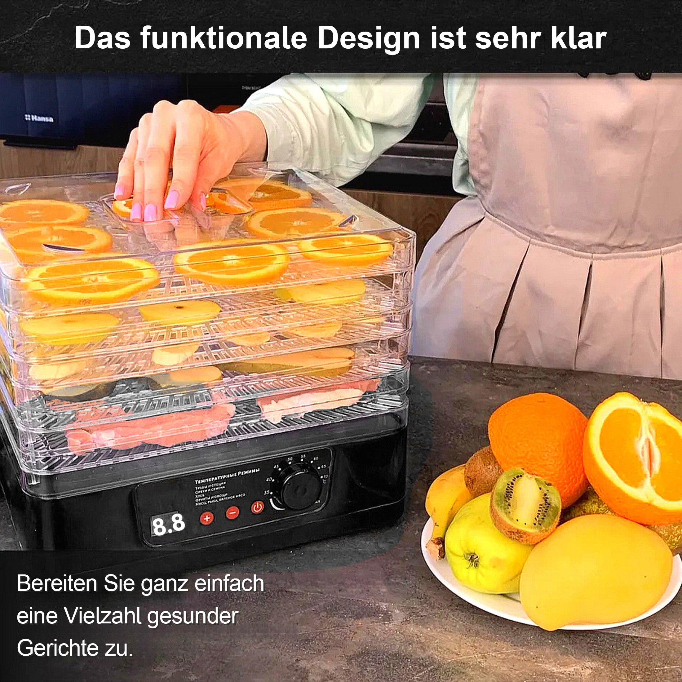 Ein Dörrgerät mit geschnittenen Orangen, Äpfeln und Fleisch. Früchte und andere Lebensmittel liegen auf einem Teller. Die Hand einer Person ist sichtbar.