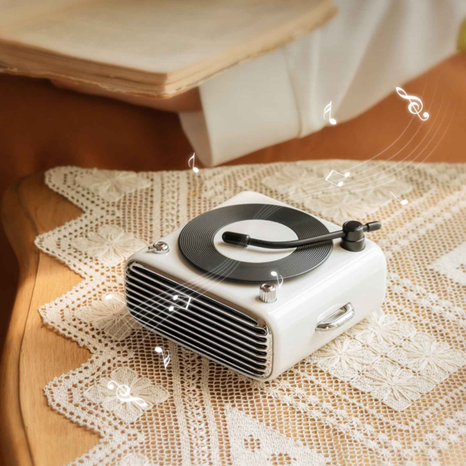 Ein weißer Plattenspieler im Retro-Stil auf einer Spitzendecke. Noten schweben darüber. Ein Buch ist im Hintergrund.