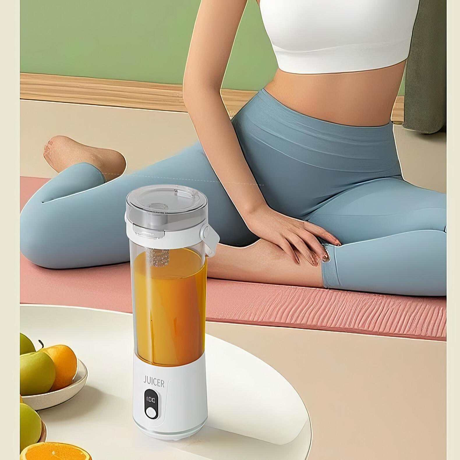 Eine Frau sitzt in der Nähe eines Entsafters mit Orangensaft. Auf einem Teller liegen Früchte. Die Frau trägt ein weißes Oberteil und blaue Leggings.