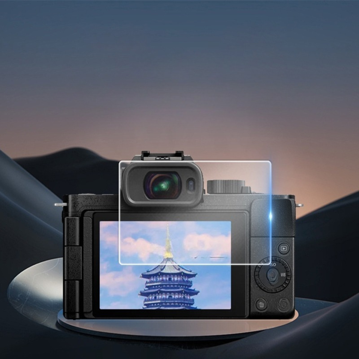 Una fotocamera nera mostra una scena di pagoda. La fotocamera poggia su una superficie scura con forme astratte contro un cielo sfumato.