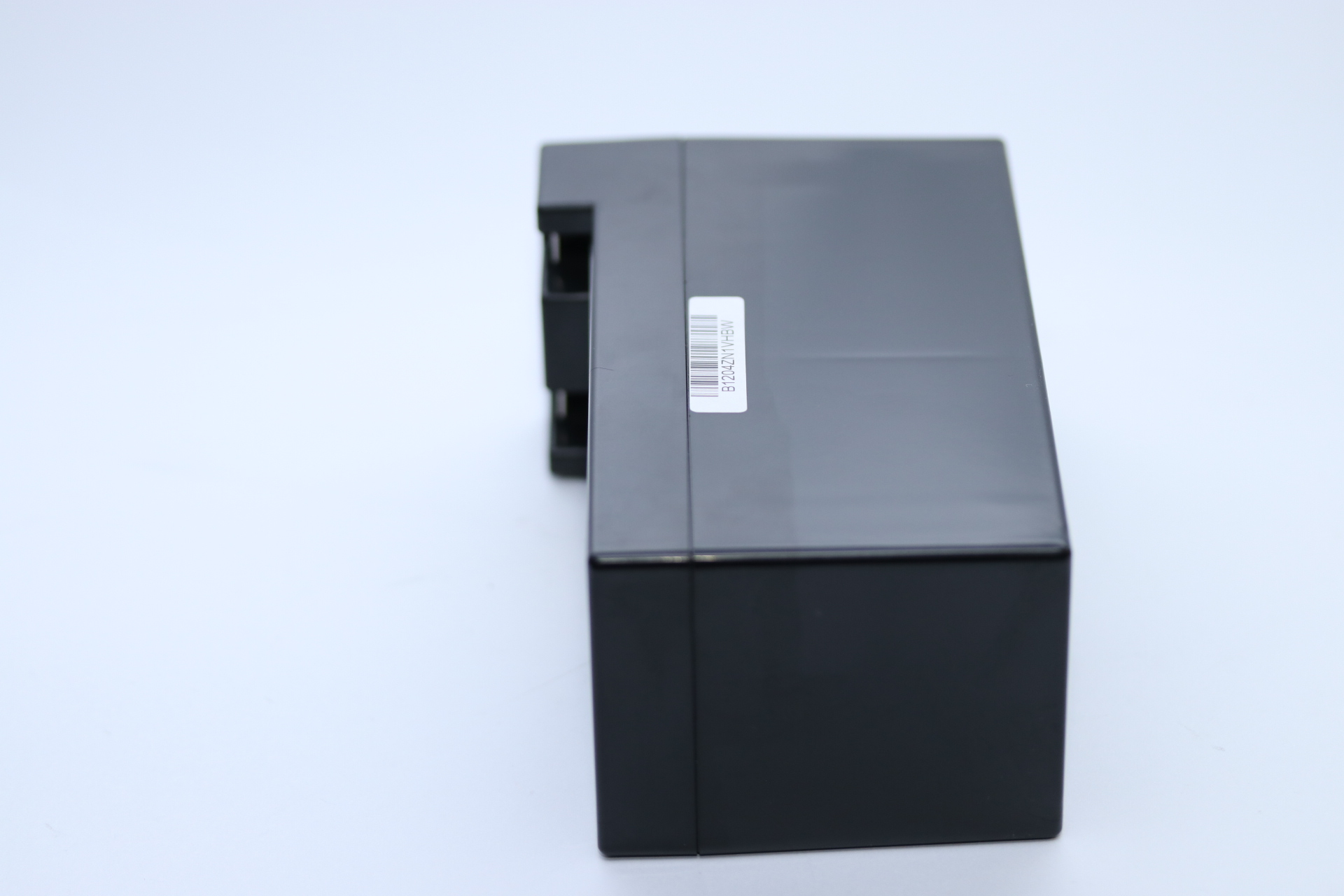 Eine schwarze rechteckige Box mit Etikett liegt auf weißer Oberfläche. Die Box ist glänzend, die Seite sichtbar.