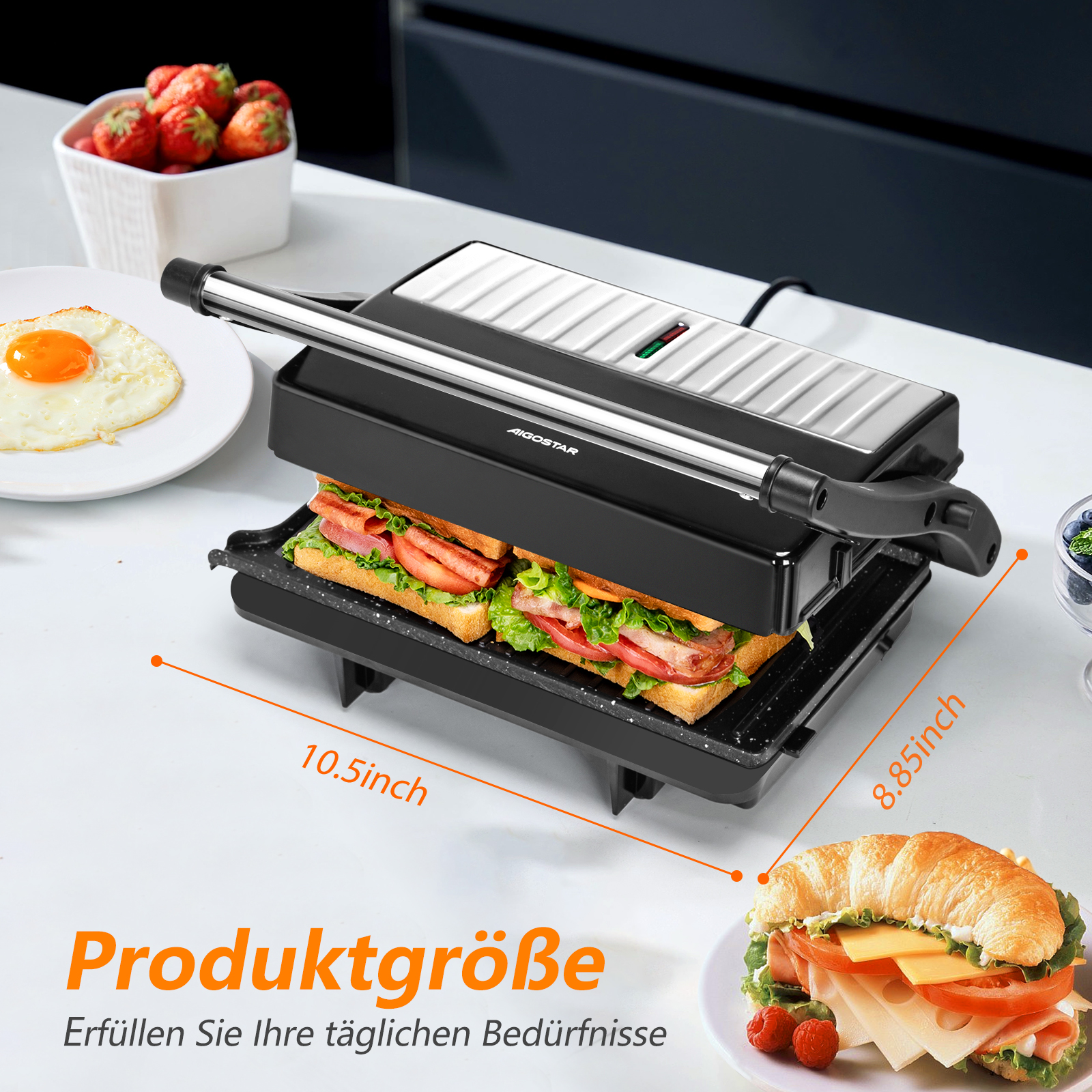 Ein Sandwichmaker mit Sandwich, ein Teller mit Spiegelei und eine Schüssel mit Erdbeeren stehen auf einer weißen Oberfläche.