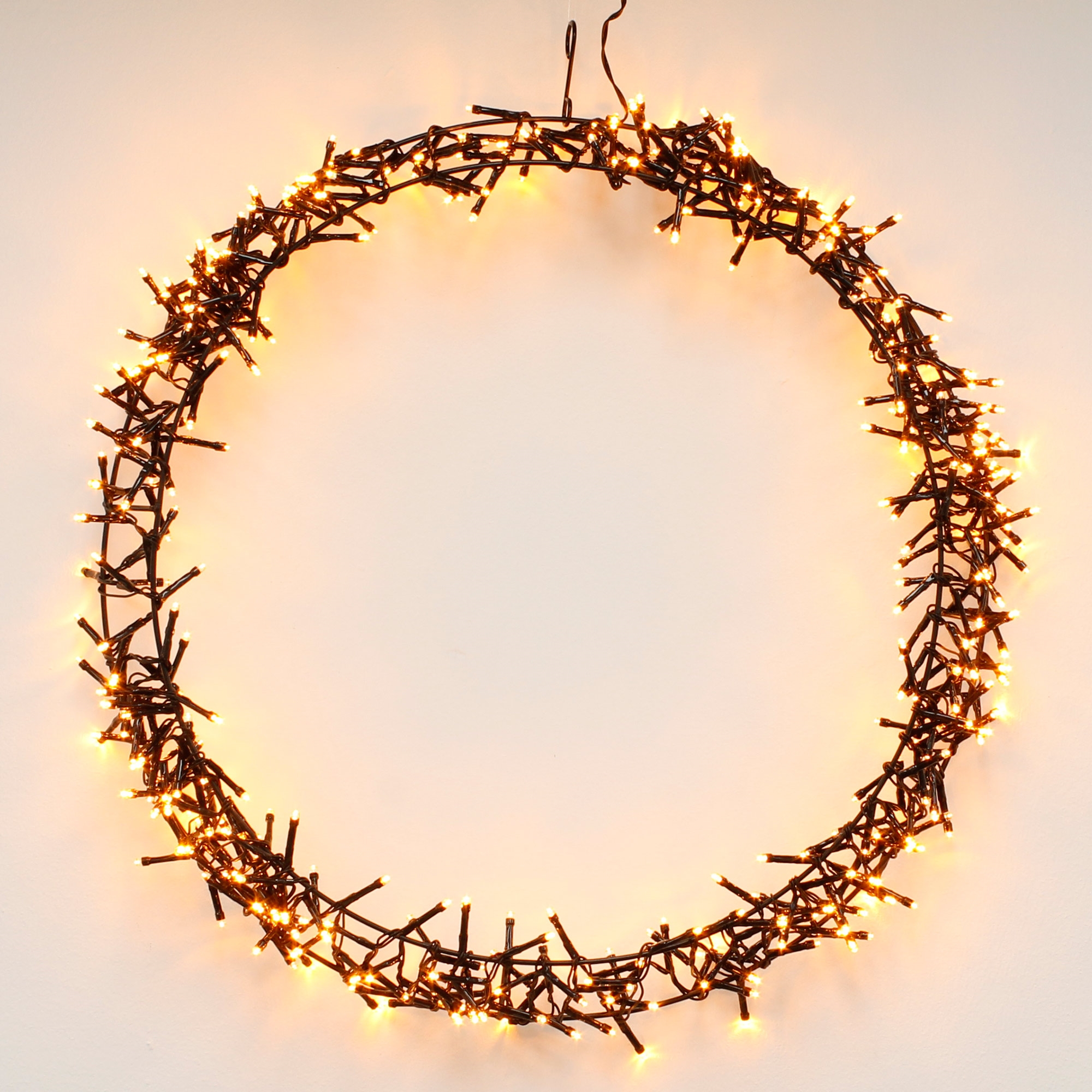 Ein kreisförmiger Weihnachtskranz aus warmweißen Lichtern vor einem weißen Hintergrund. Die Lichter sind an, die Drähte sind dunkel.