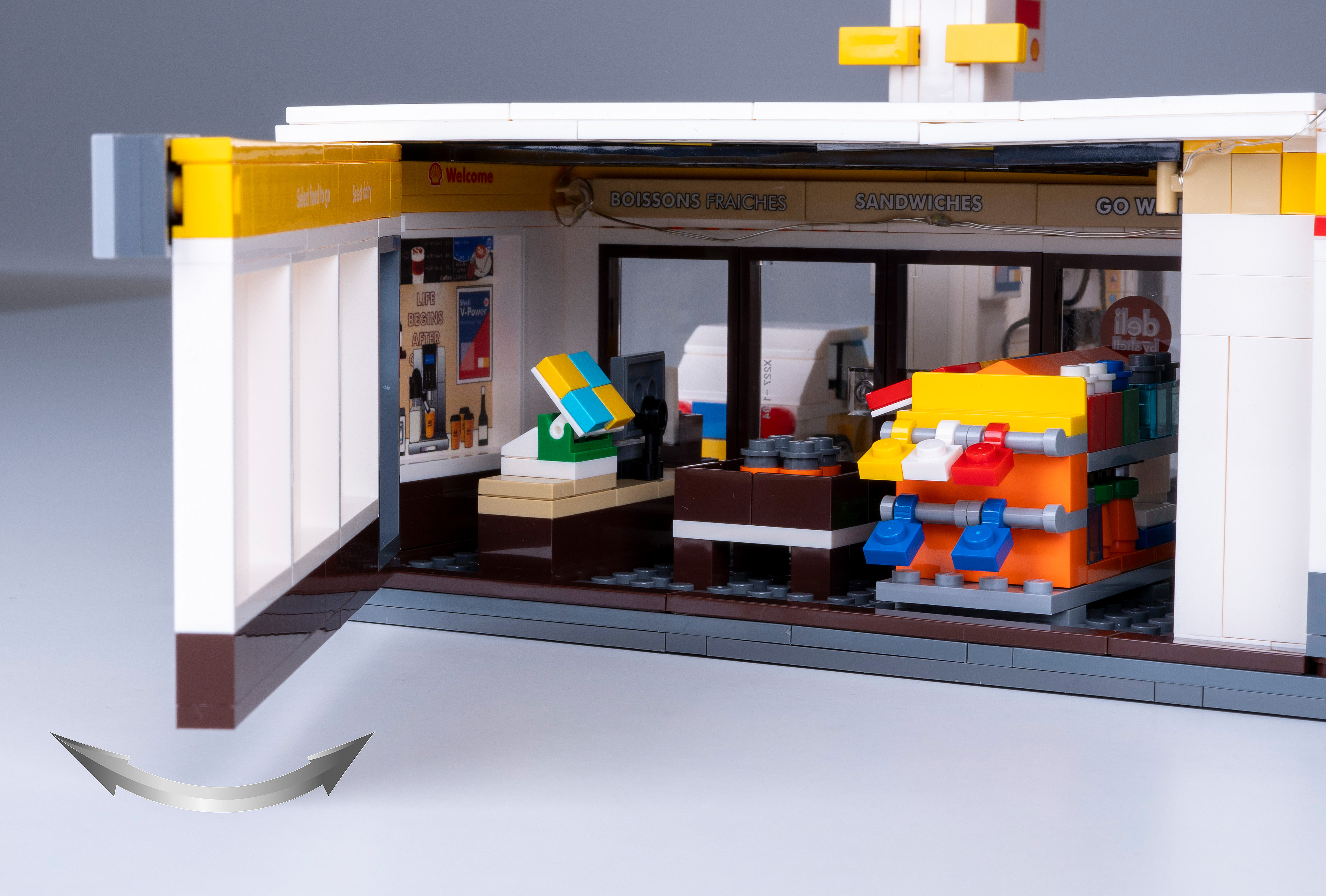 Ein Lego-Tankstelleninnenraum mit Schildern, Auslagen und Servicetheken. Draußen ist eine weiße und gelbe Fassade.