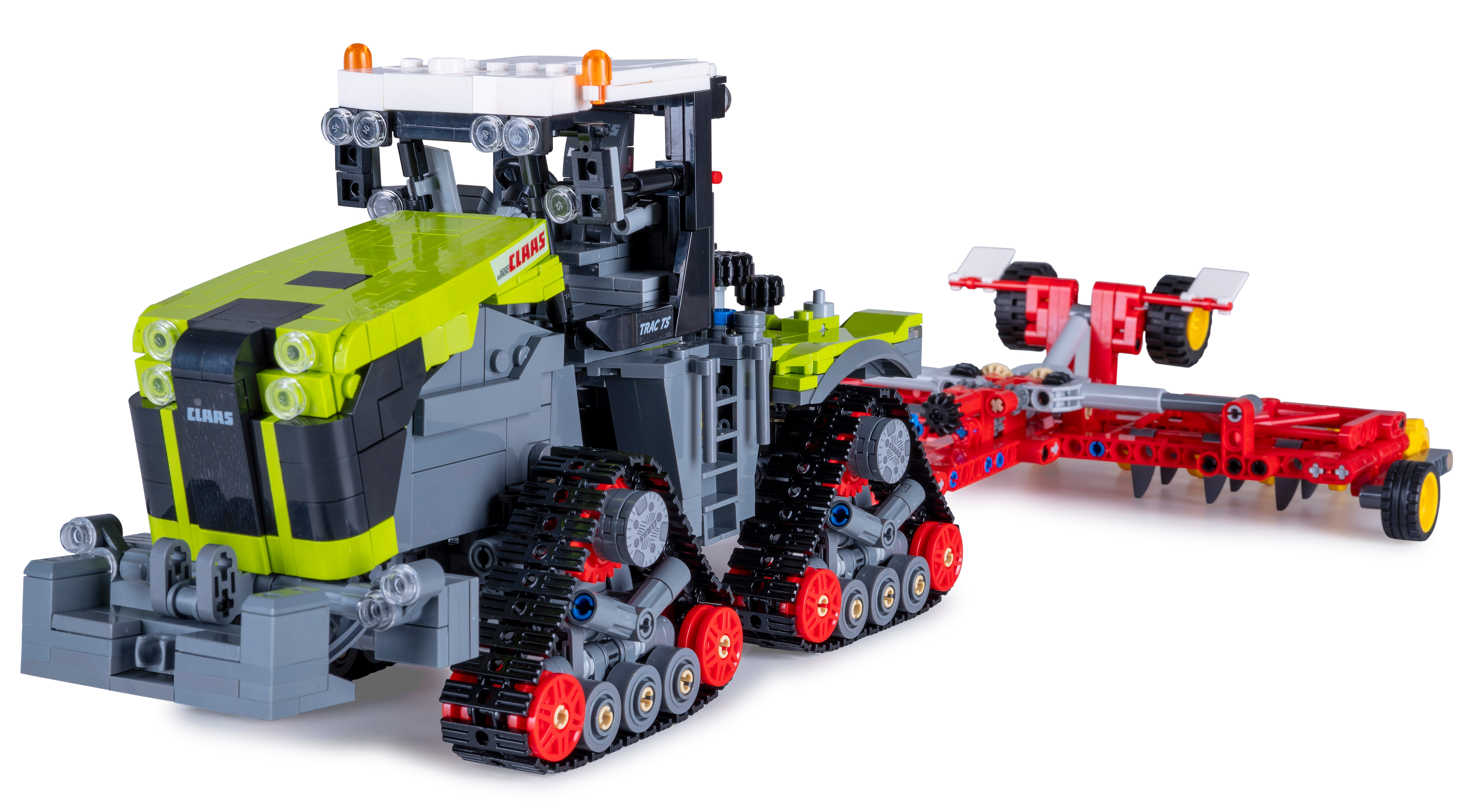 Ein Claas-Traktorspielzeug mit einem rot-schwarzen Anhänger aus Legosteinen. Der Traktor ist grün und grau.