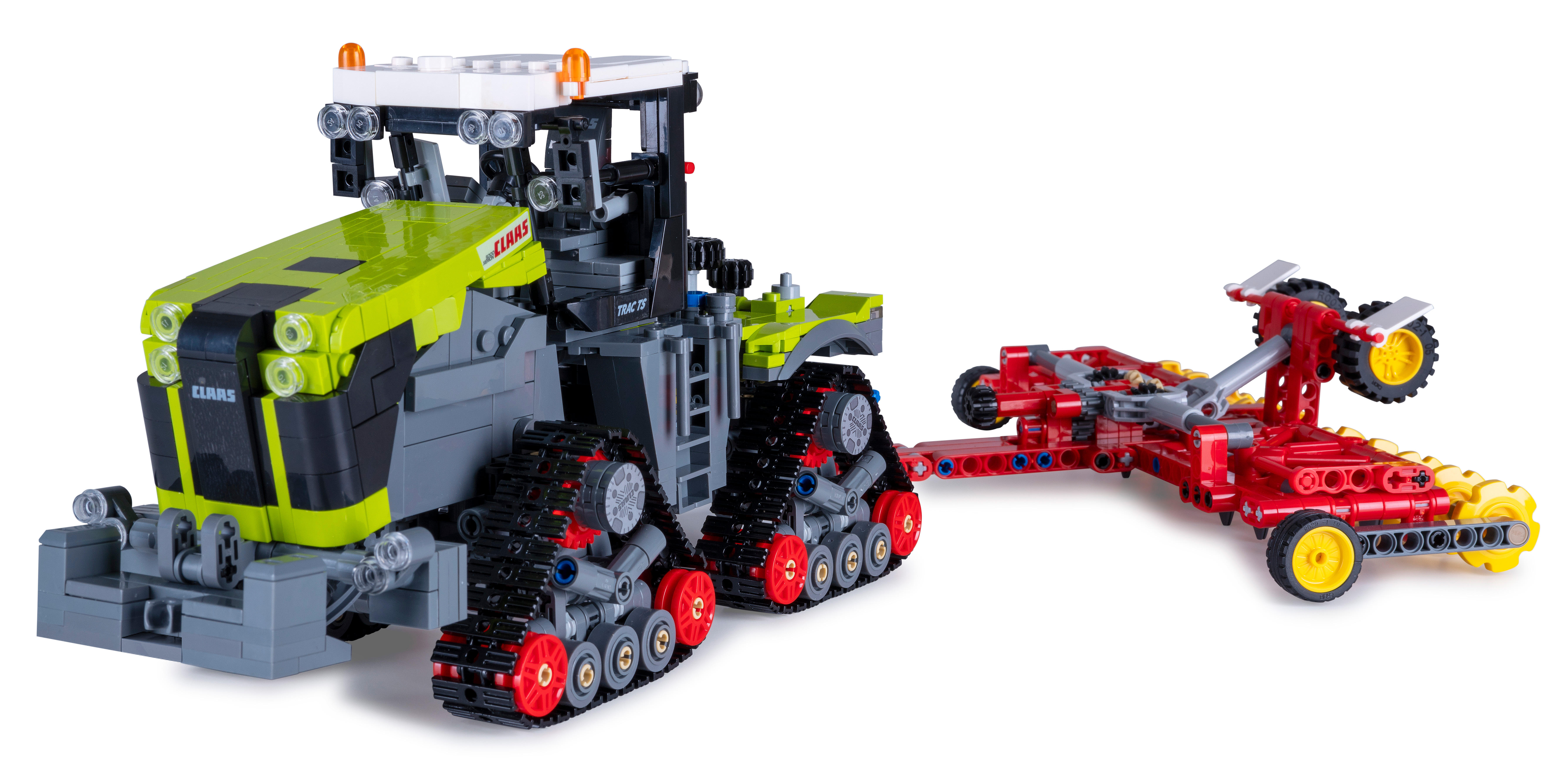 Ein Lego Claas Traktor und sein roter Anhänger auf weißem Hintergrund. Der Traktor hat grüne und graue Teile.