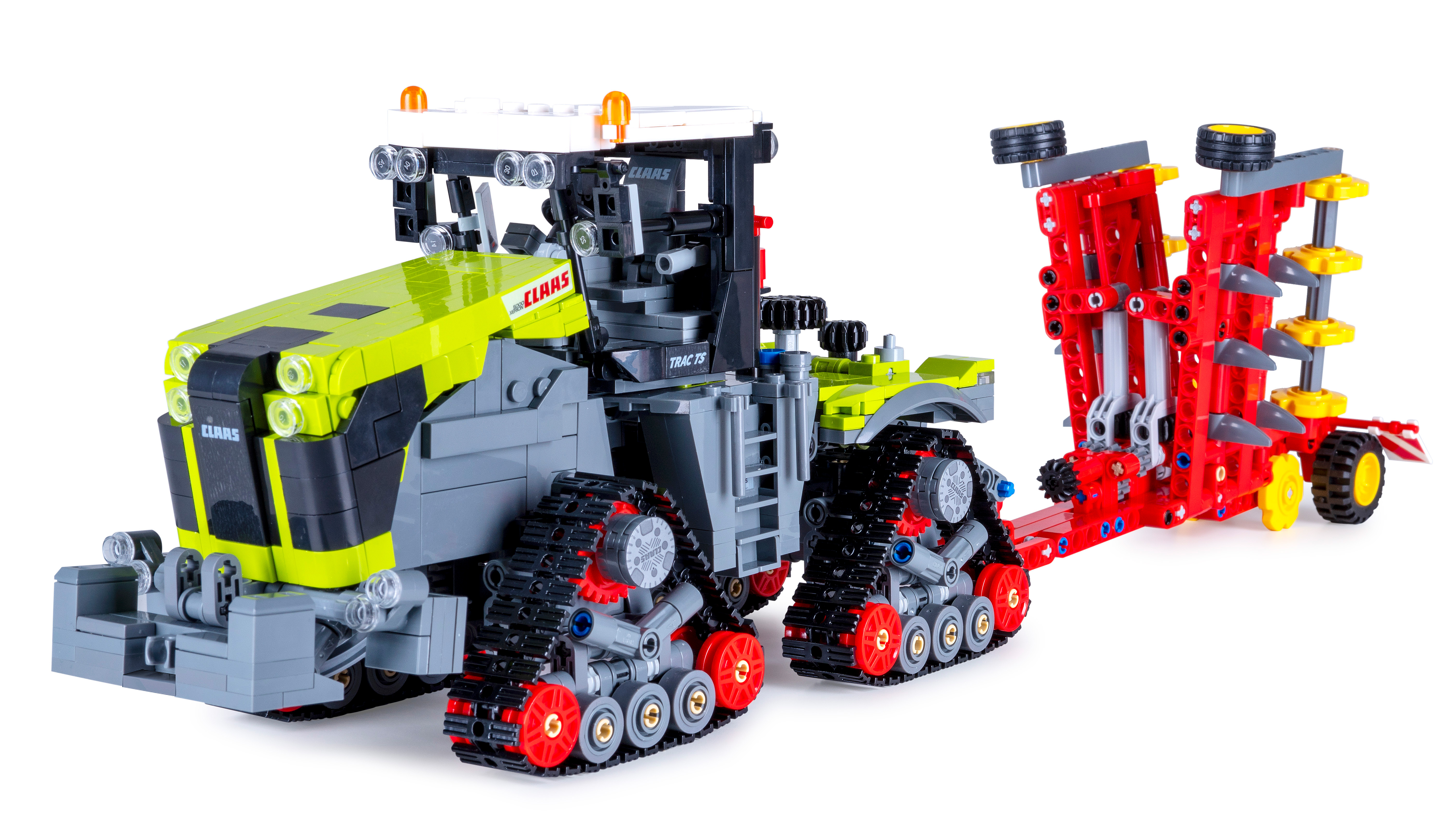 Ein Claas Lego-Traktormodell mit Ketten und einem Pflug. Der Traktor ist grau und grün, der Pflug rot.