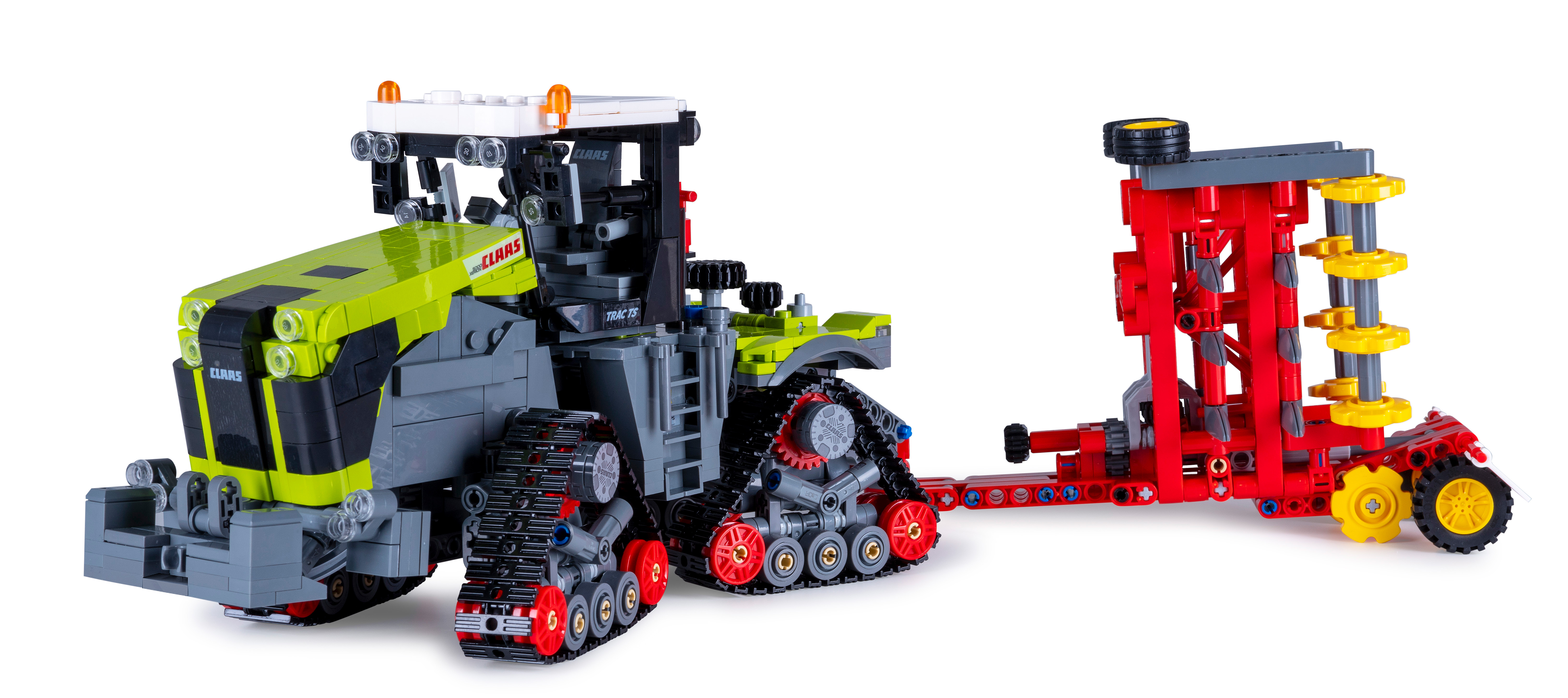 Ein Claas-Traktorspielzeug mit rotem Anbaugerät. Der Traktor ist grün und grau, das Anbaugerät ist rot und gelb. Weißer Hintergrund.