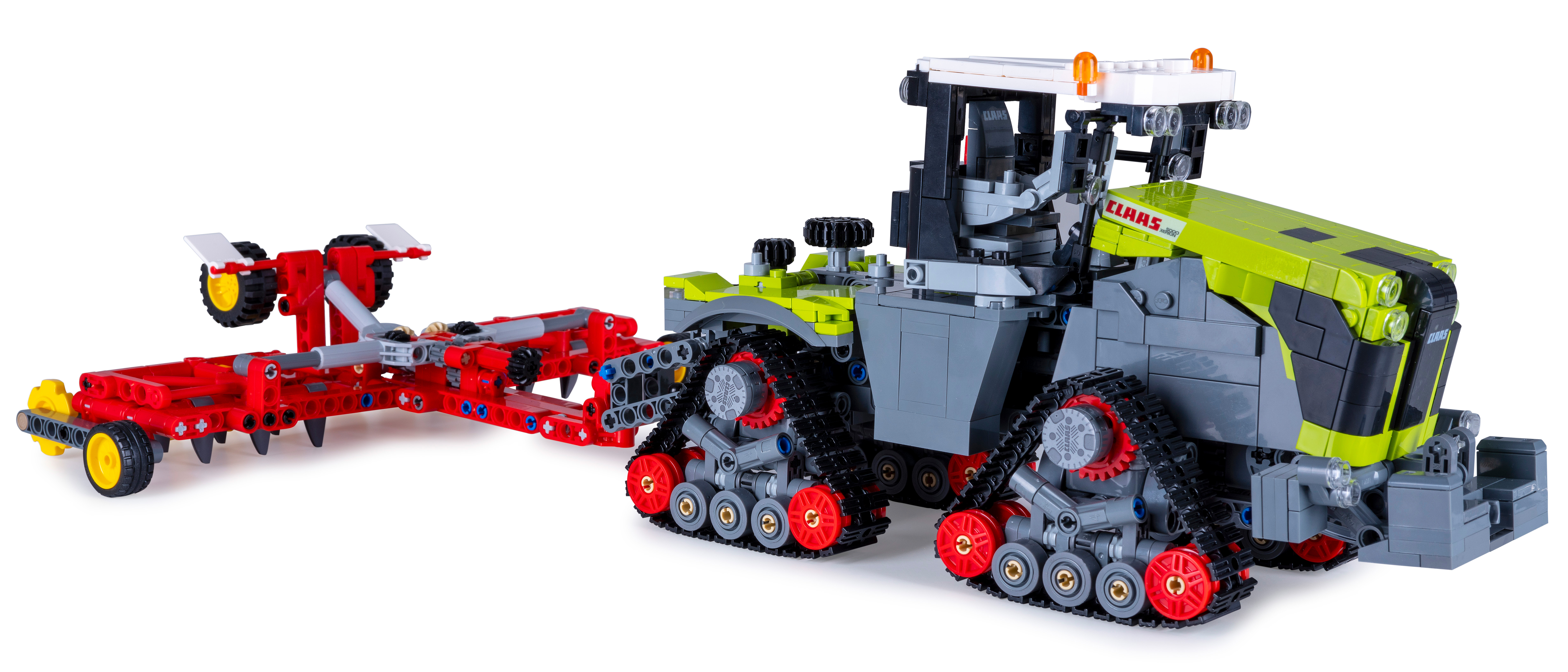 Ein Lego Claas Traktor mit rotem Anhänger. Der Traktor ist grau und lindgrün mit schwarzen Ketten. Der Anhänger ist rot.