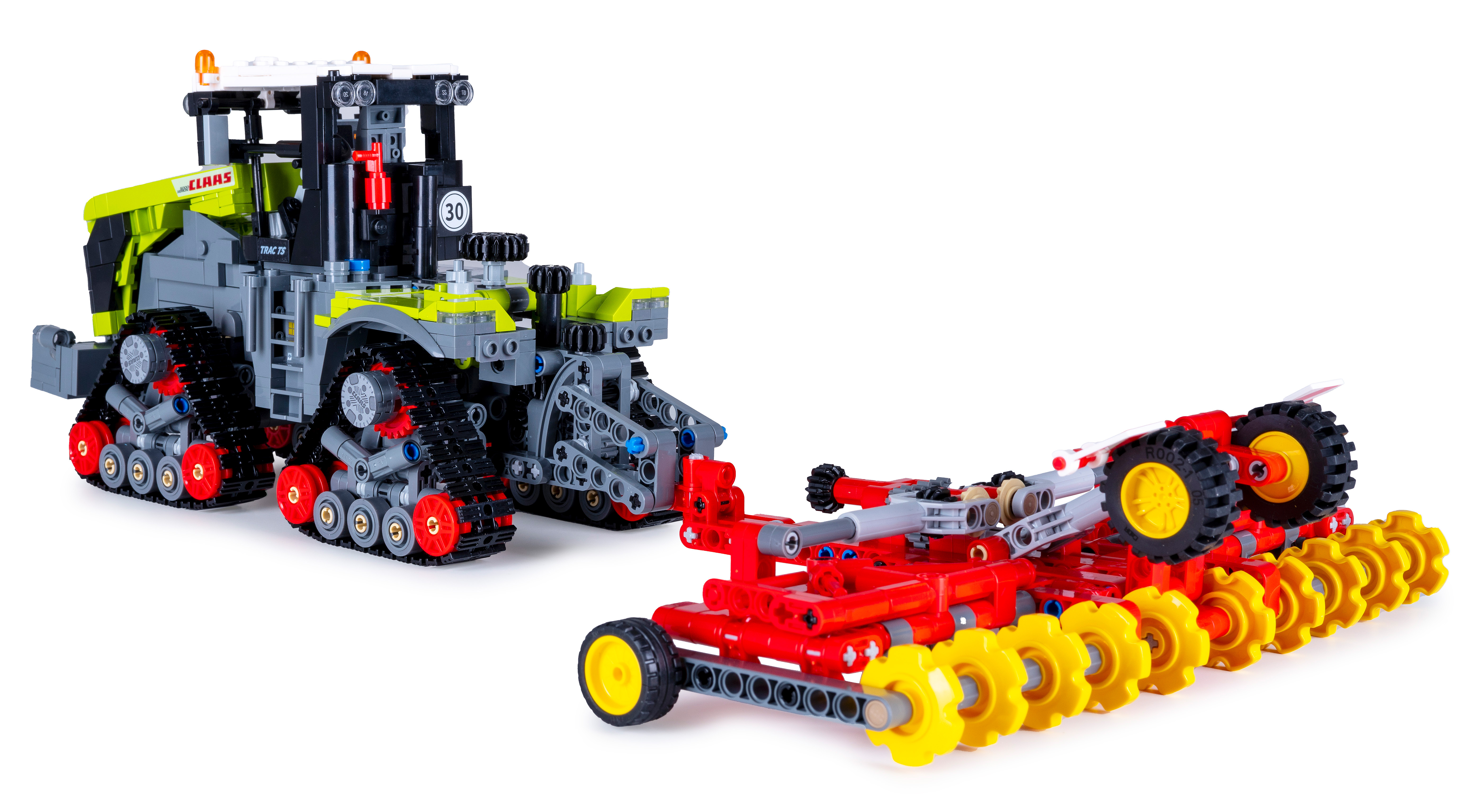 Ein Claas-Traktorspielzeug mit einem roten und gelben Pflug. Der Traktor ist grau, schwarz und grün. Sie stehen vor einem weißen Hintergrund.