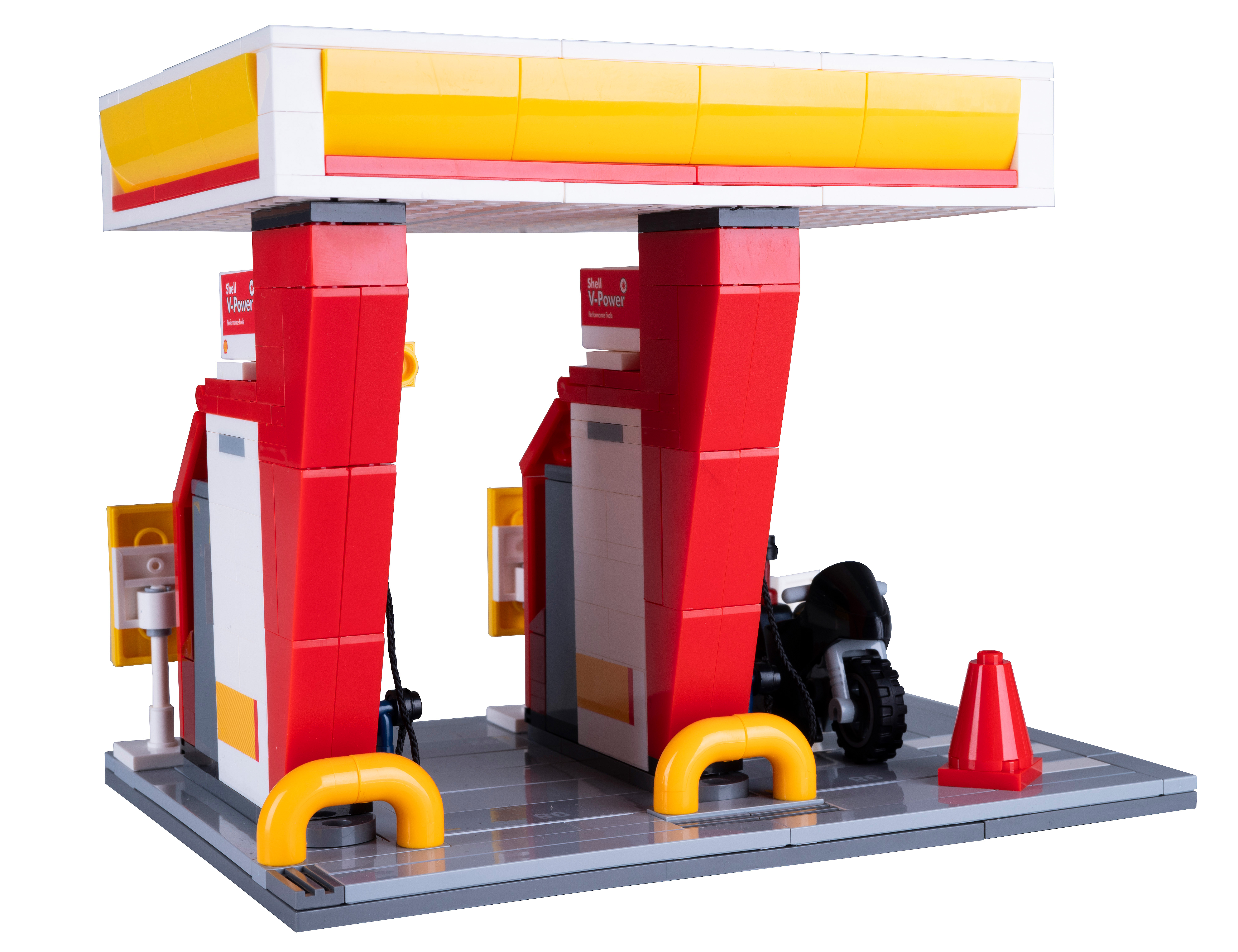 Eine Lego-Tankstelle mit roten, weißen und gelben Farben. Ein schwarzes Motorrad und ein roter Kegel sind ebenfalls zu sehen.