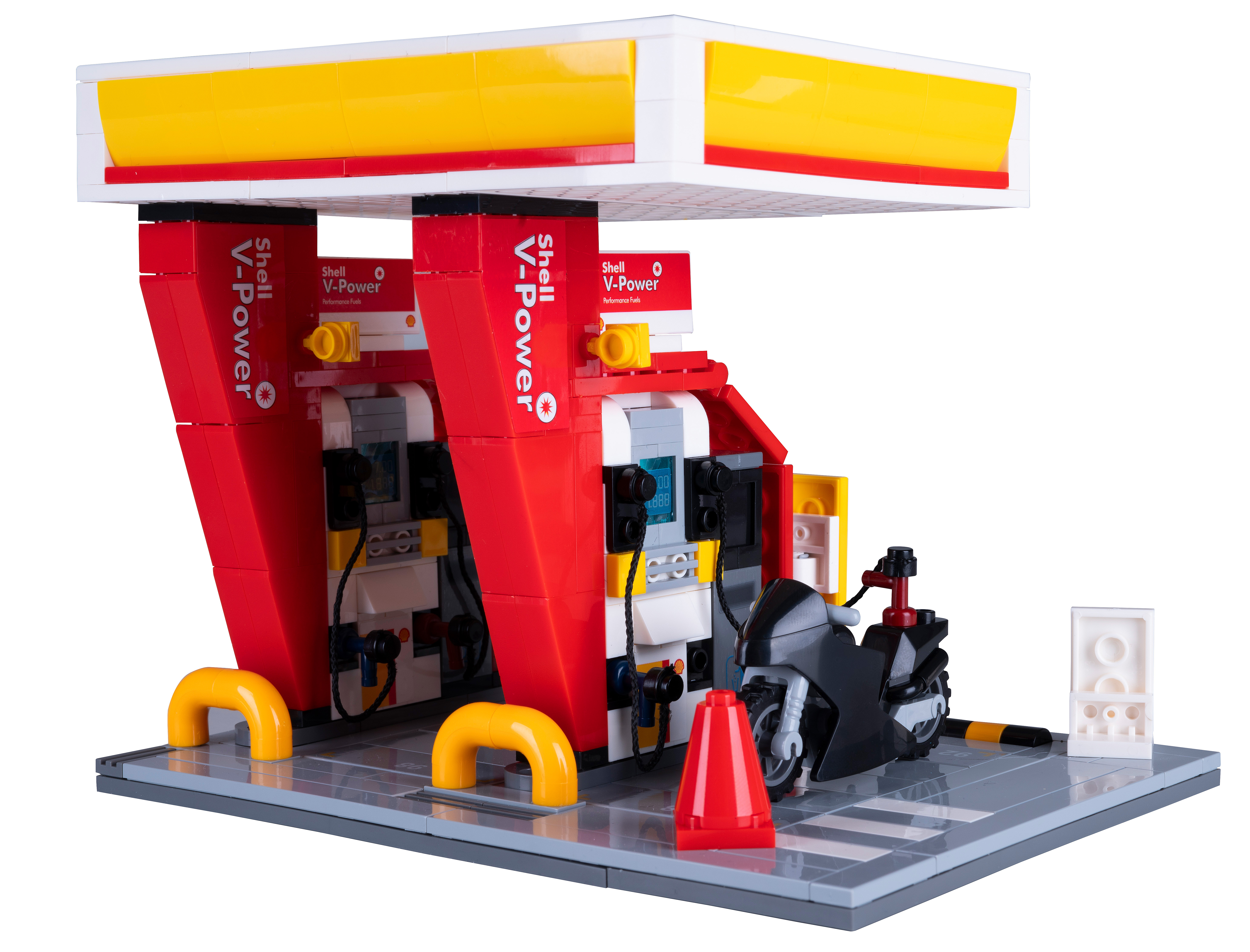 Eine LEGO Shell-Tankstelle mit einem schwarzen Motorrad, einem roten Kegel und einem weiß-gelben Vordach.