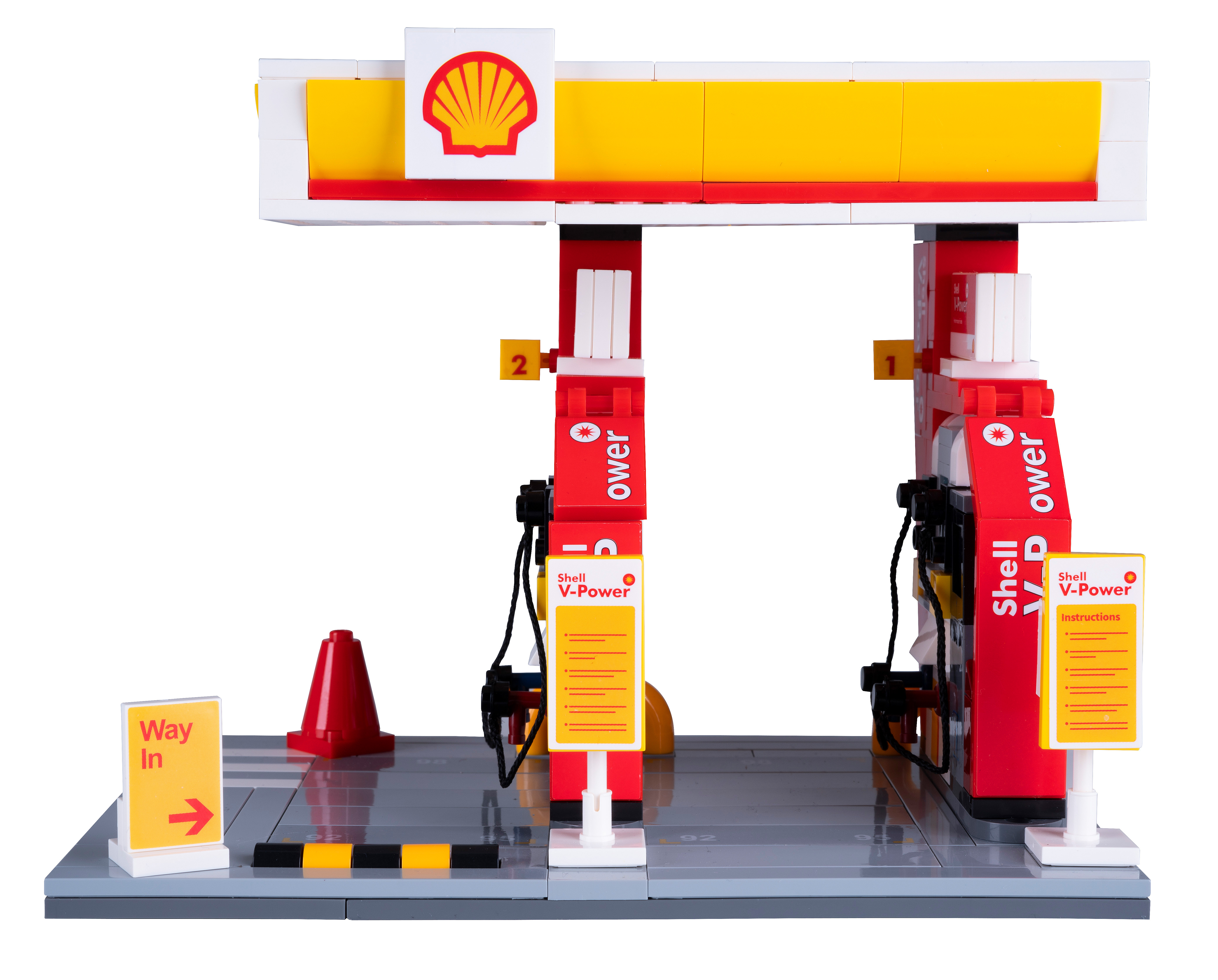 Ein Lego-Modell einer Shell-Tankstelle. Es hat ein weiß-gelbes Vordach, rote Zapfsäulen und ein "Way In"-Schild. Ein roter Kegel ist platziert.