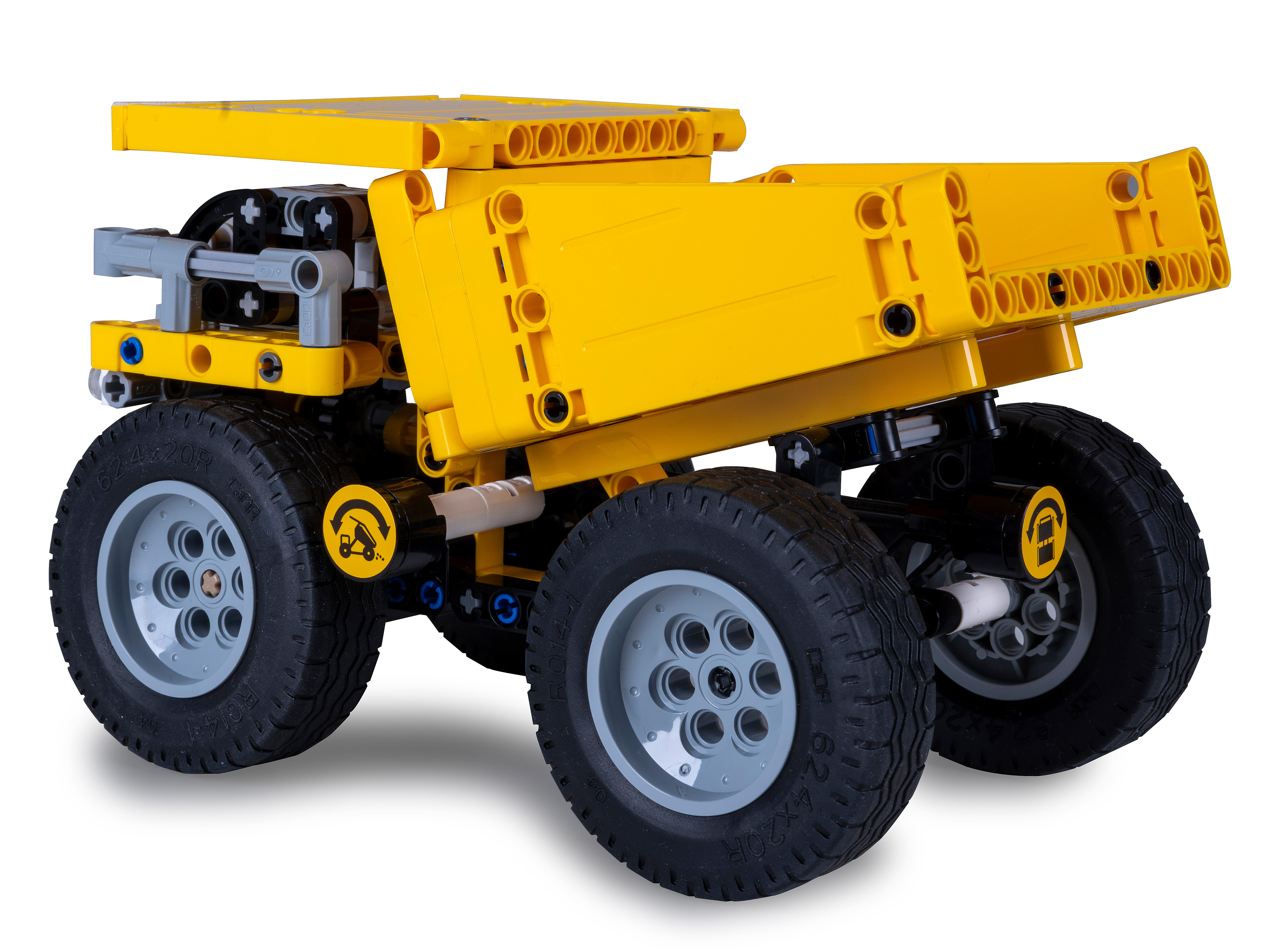 Ein gelber Lego-Muldenkipper mit schwarzen Reifen und grauen Radnaben vor weißem Hintergrund.