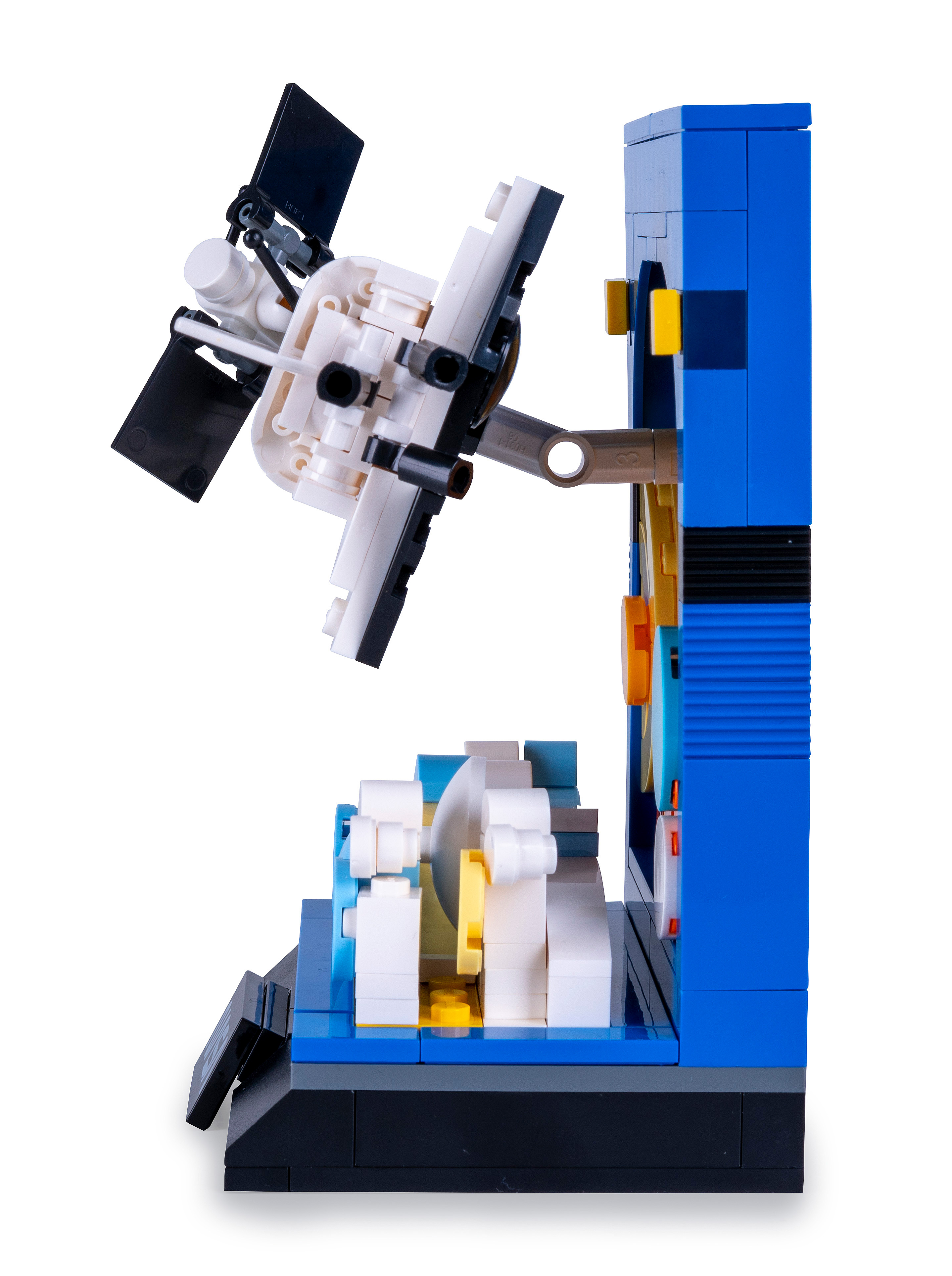 Ein LEGO-Modell einer Maschine mit blauen, weißen und gelben Blöcken. Ein Satellit ist an der Maschine befestigt.