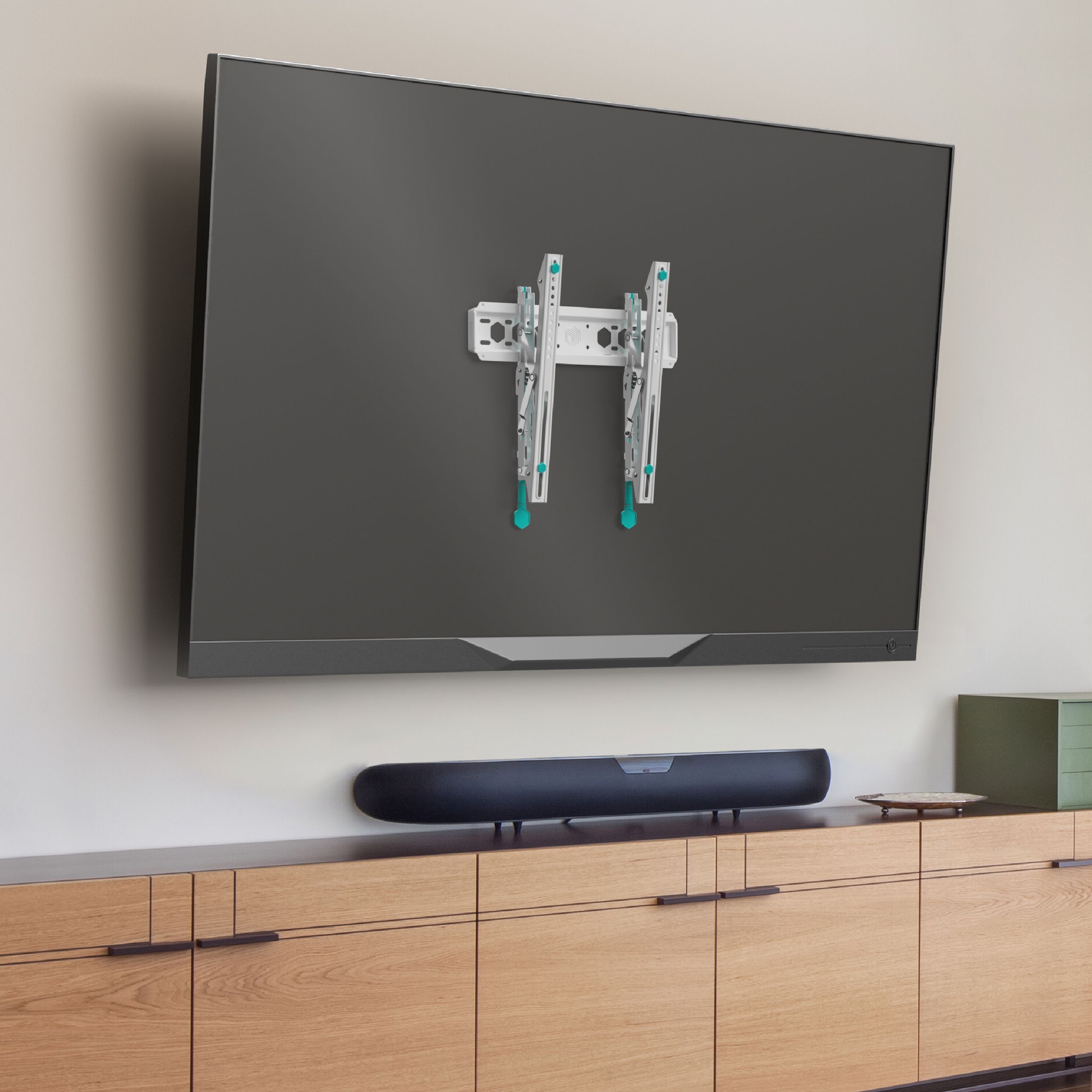 Telewizor zamontowany na ścianie z soundbarem poniżej. Pod soundbarem znajduje się drewniana szafka. Widoczny jest uchwyt TV.