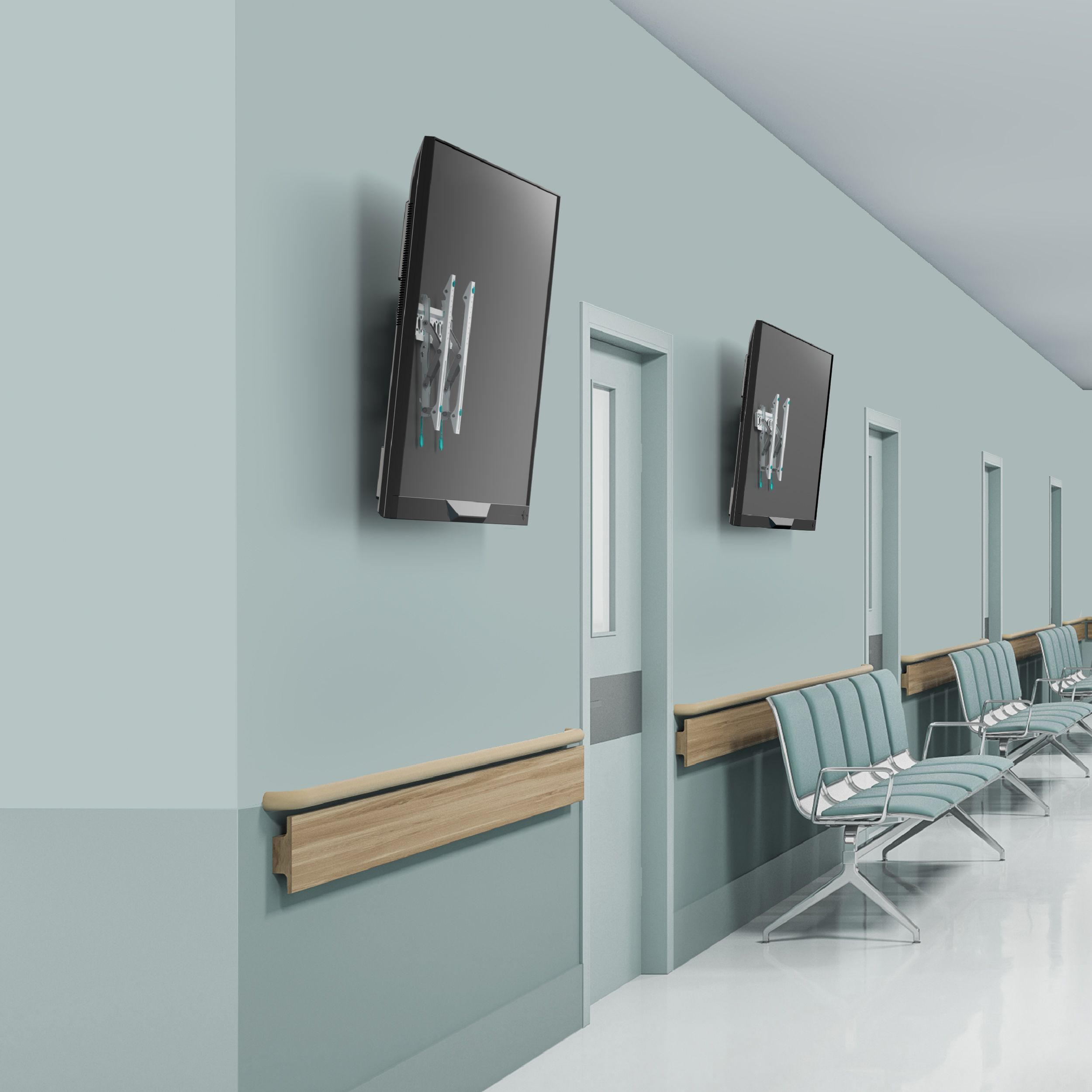 Korytarz szpitalny z dwoma zamontowanymi telewizorami, drzwiami, poręczami i krzesłami. Ściany są jasnozielone.