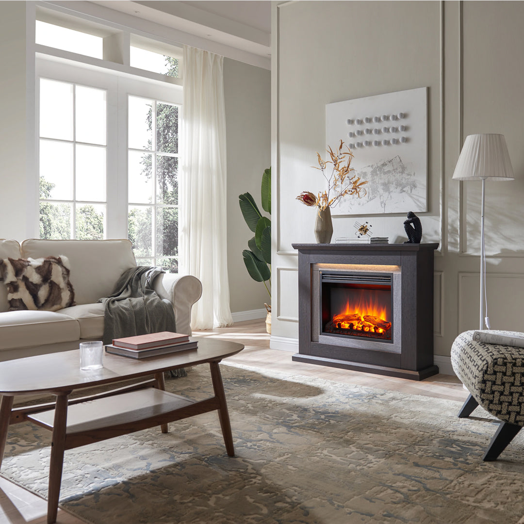 Ein Wohnzimmer mit Kamin, Sofa, Couchtisch und Fenster. Ein Teppich bedeckt den Boden. Eine Lampe und ein Stuhl befinden sich rechts.