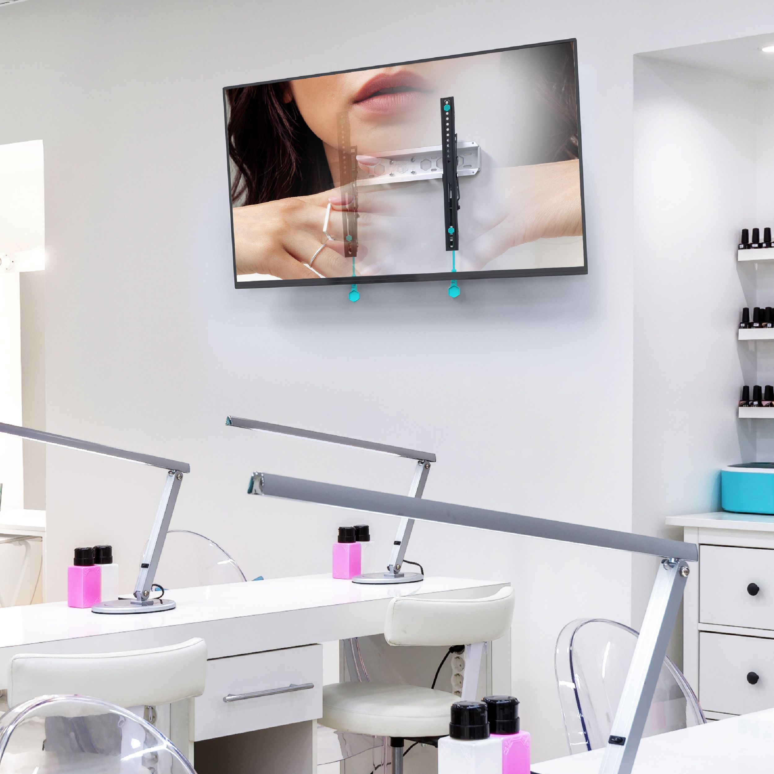 Wnętrze salonu paznokci. Telewizor wyświetla model dłoni, stoły z lampami, krzesła i lakier do paznokci.