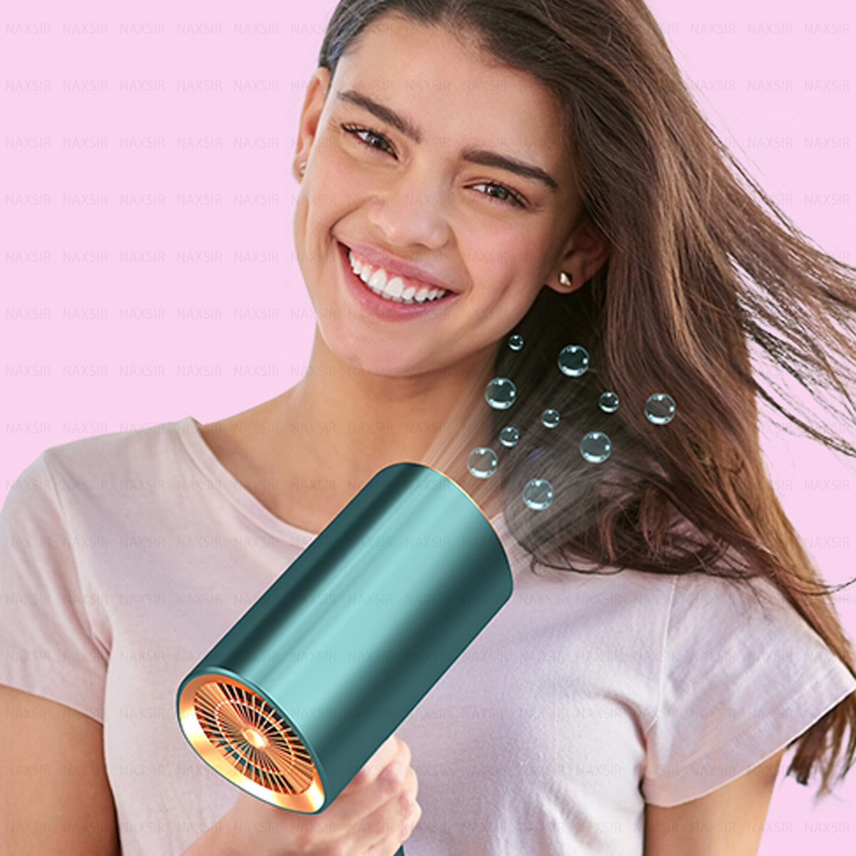 Una donna sorride, usa un asciugacapelli verde acqua. I capelli volano. Bolle fluttuanti. Sfondo rosa.