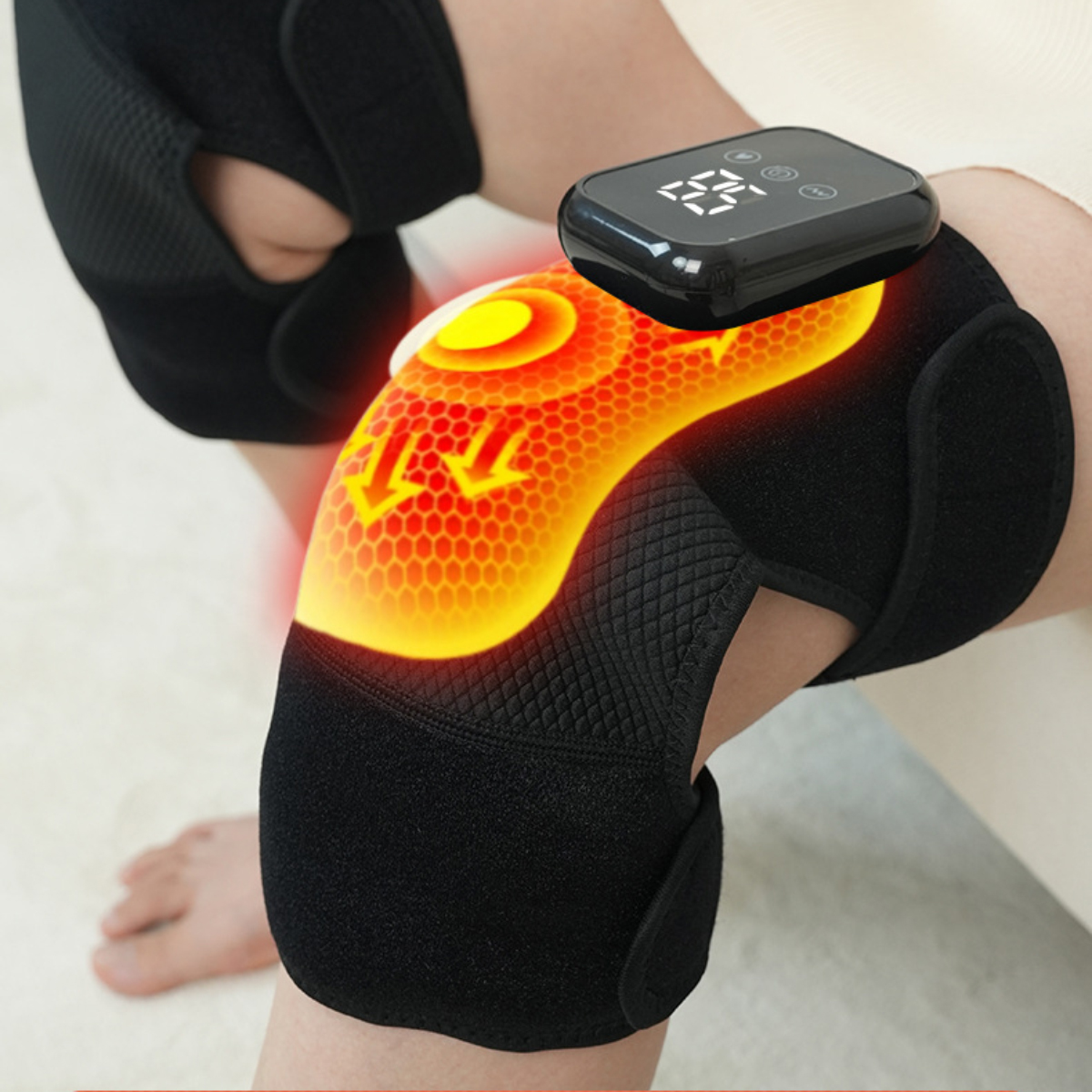 Ein Knie einer Person mit einer schwarzen Wärmeumwicklung. Ein glühendes, oranges Design zeigt die Wärmeapplikation an. Ein kleines schwarzes Gerät liegt oben auf.