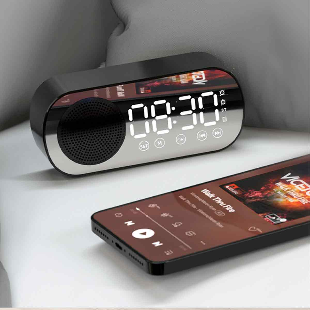 Schwarze Digitaluhr mit der Anzeige 08:30, neben einem Smartphone, das Musik abspielt. Der Hintergrund ist ein weiches Kissen.