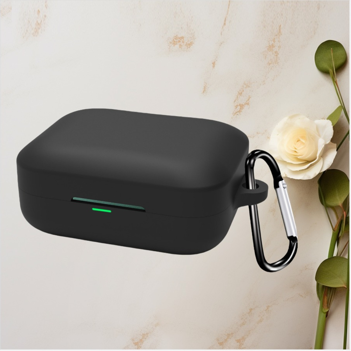Custodia nera per auricolari con luce verde, moschettone, rosa bianca e foglie verdi su sfondo marmoreo.