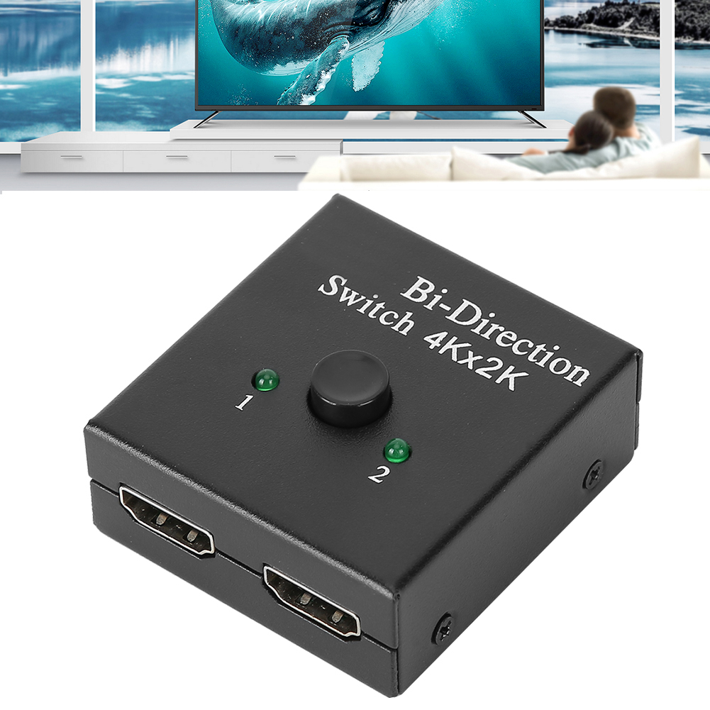 Schwarzer HDMI-Switch mit grünen LEDs, beschriftet mit 'Bi-Direction Switch 4Kx2K'. Hintergrund zeigt TV mit Wal, Leute auf Couch.