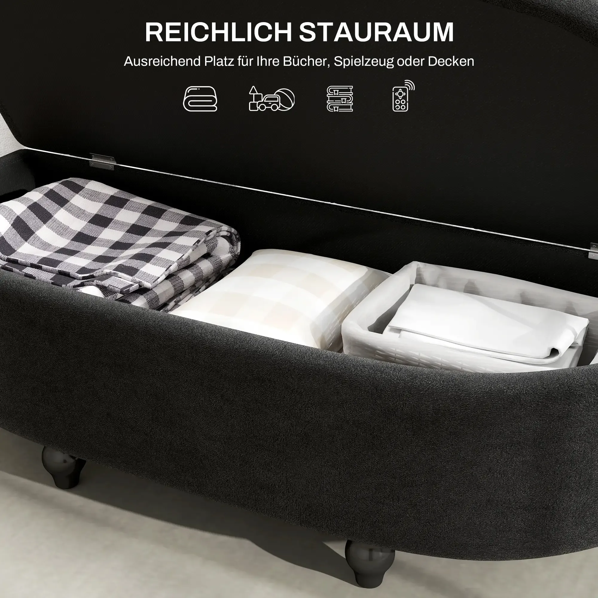 Offene schwarze Aufbewahrungsbank gefüllt mit Decke, Kissen und Korb. Text oben sagt 'Viel Stauraum'.