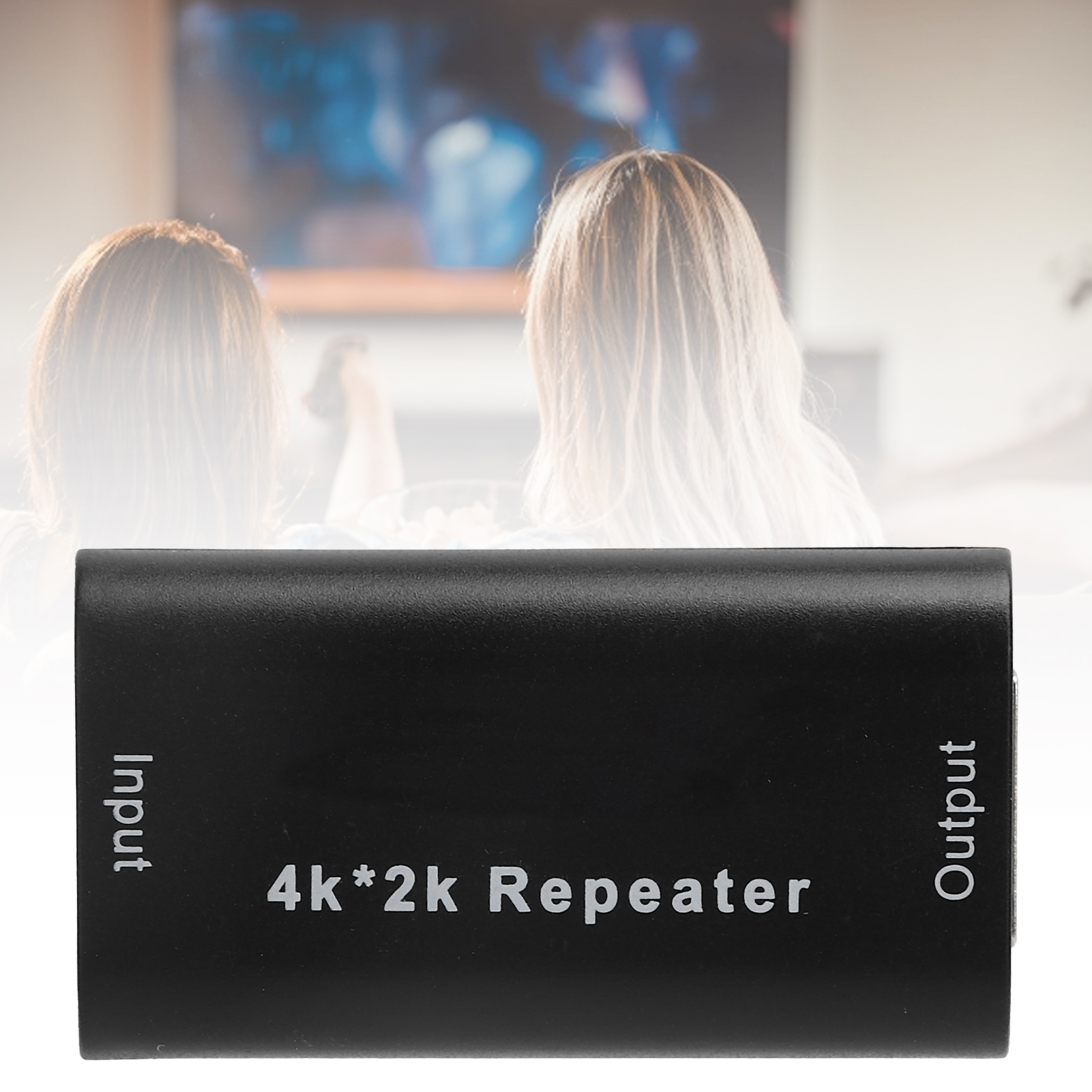 Ein schwarzer 4K*2k-Repeater mit den Aufschriften Input und Output steht im Mittelpunkt. Im Hintergrund schauen zwei Personen fern.