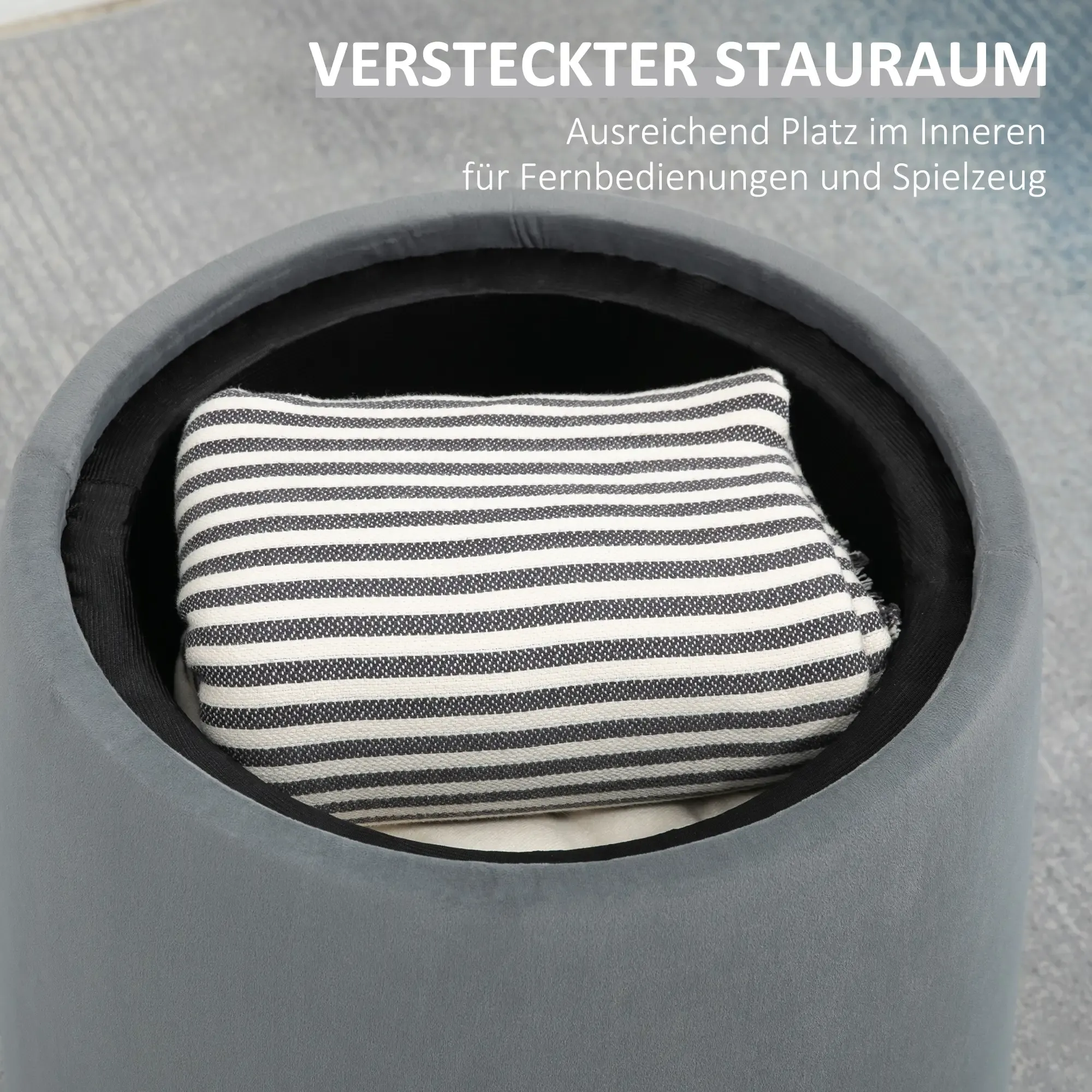 Graue Aufbewahrungshocker mit gestreiftem Kissen. Der Hocker hat eine schwarze Innenseite und steht auf einer grauen Oberfläche.