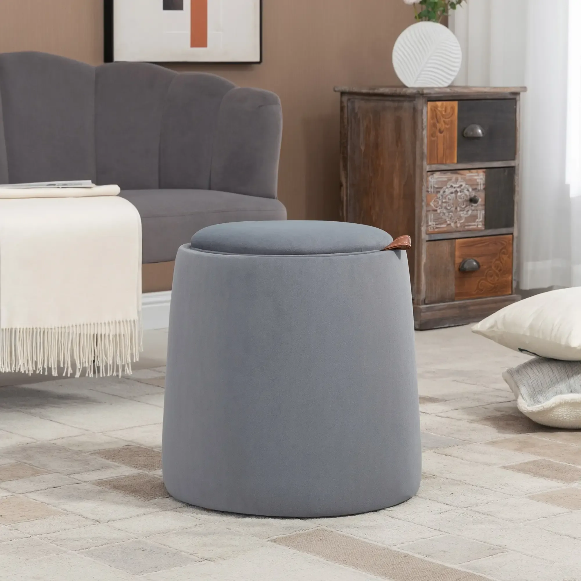Ein grauer Hocker mit grauem Deckel steht auf einem gemusterten Teppich. Im Hintergrund sind ein Sofa und ein Holzschrank.
