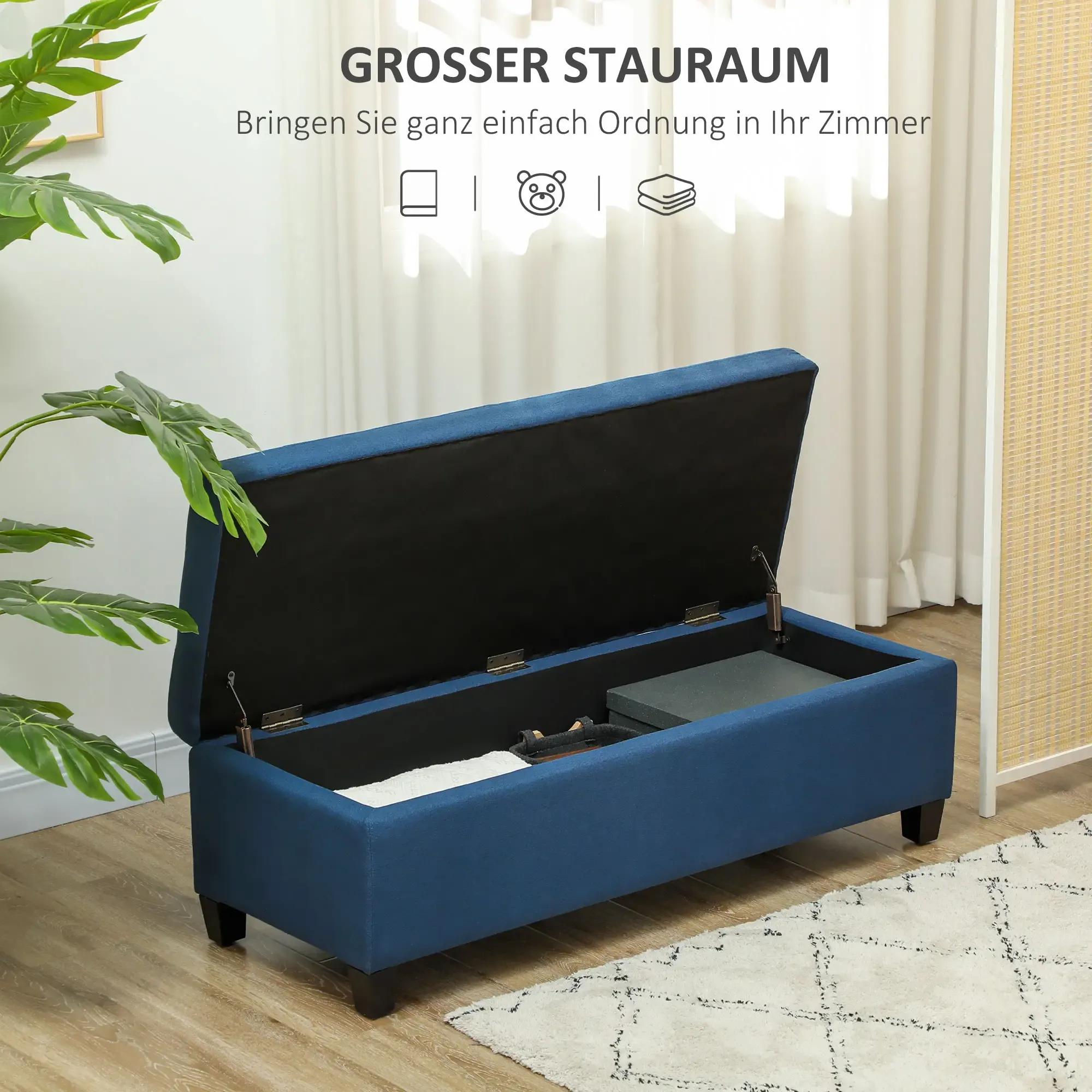 Offene blaue Aufbewahrungsbank mit Gegenständen im Inneren, auf einem Teppich in der Nähe einer Pflanze und eines gewebten Schirms.