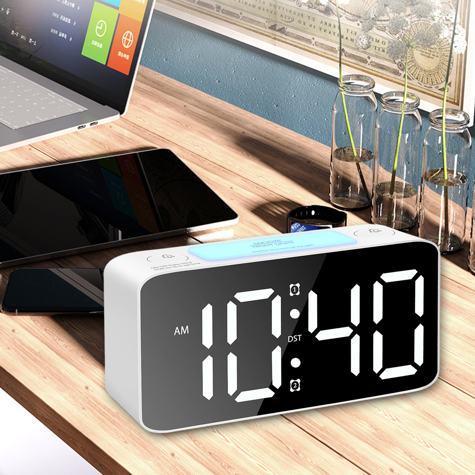Eine Digitaluhr zeigt 10:40 Uhr an. Auf einem Holztisch liegen Laptop, Tablet und drei Glasvasen.