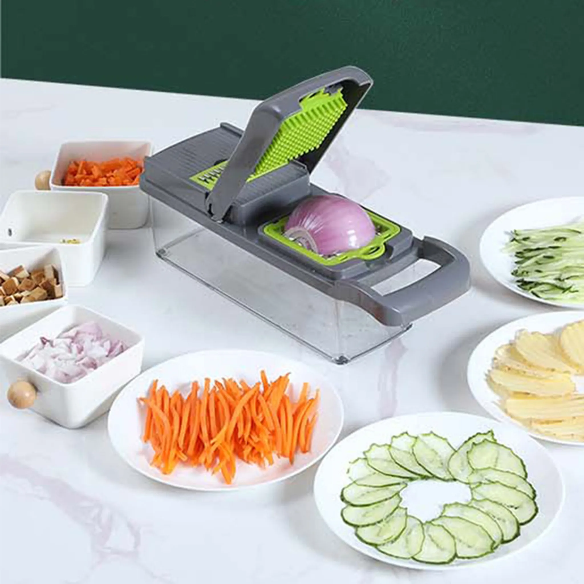 Ein Gemüseschneider mit einer Zwiebel darin. Geschnittene Karotten, Gurken und Kartoffeln liegen auf Tellern. Weiße Behälter mit gehacktem Gemüse.