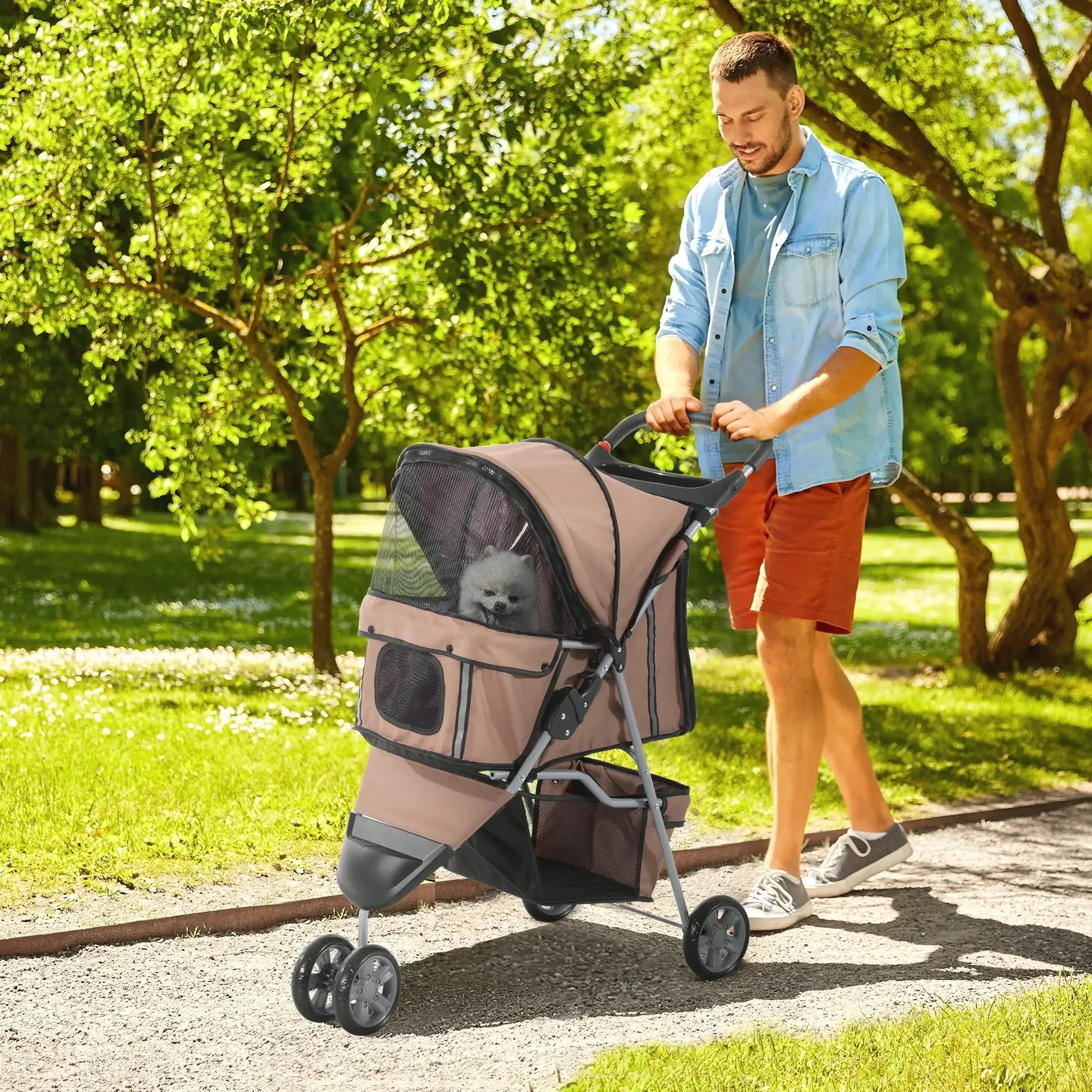 Ein Mann schiebt einen Kinderwagen für Hunde in einem Park. Ein kleiner Hund ist darin. Bäume und Grün umgeben sie.
