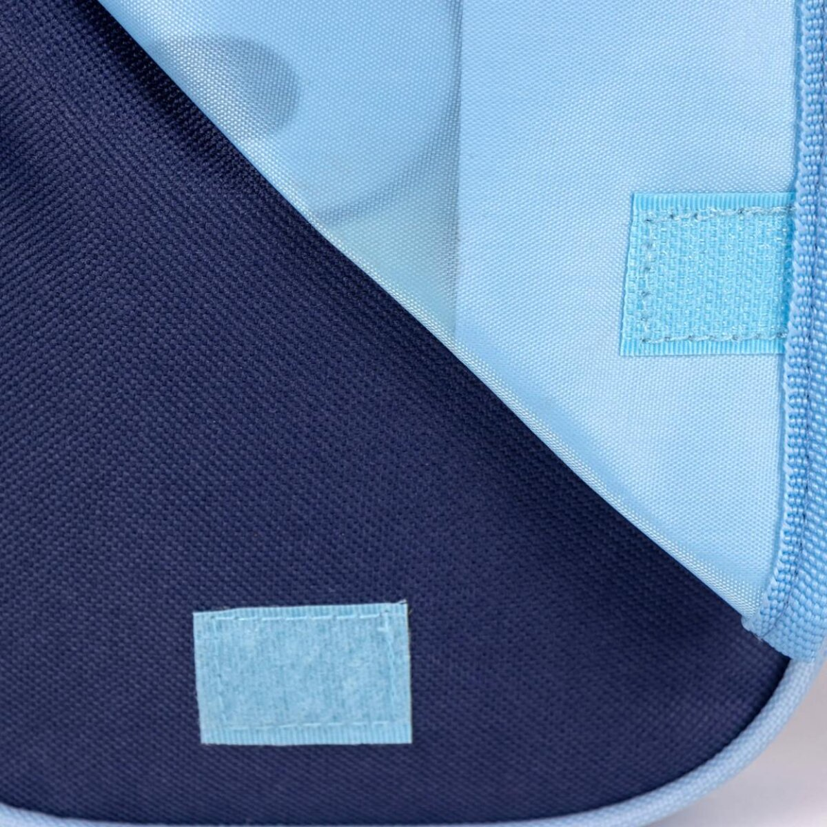 Primer plano de un estuche azul y marino parcialmente abierto. Tiene dos parches de velcro y una cremallera.