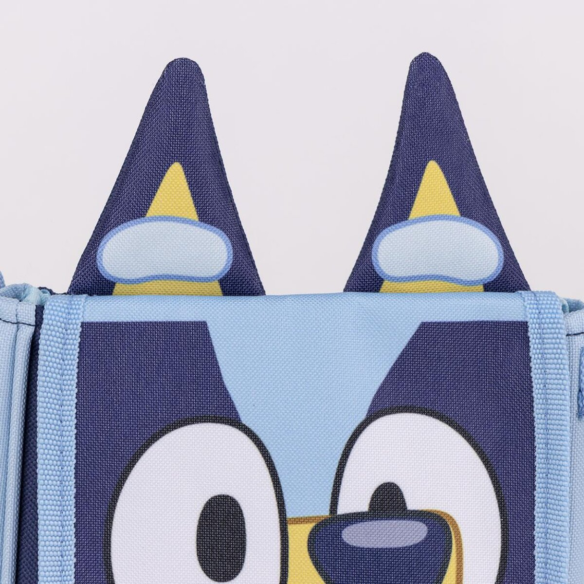 Primer plano de la cara de un perro de dibujos animados, con ojos grandes, orejas azules con detalles amarillos y blancos y fondo azul claro.