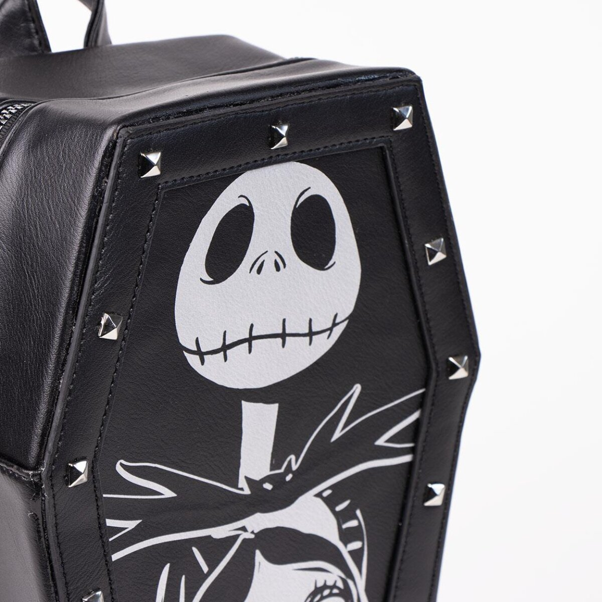 Mochila negra en forma de ataúd con la cara de Jack Skellington en blanco. Tachuelas delinean la forma del ataúd. Asa y cremallera son visibles.