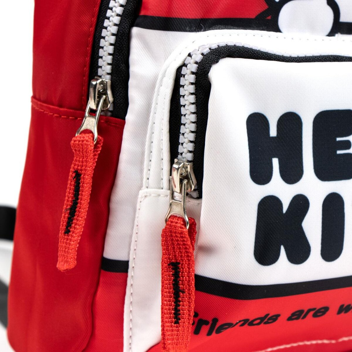 Mochila roja y blanca de Hello Kitty. Cuenta con cremalleras, contorno negro y una lengüeta roja. La mochila tiene las palabras 'Hello Kitty'.