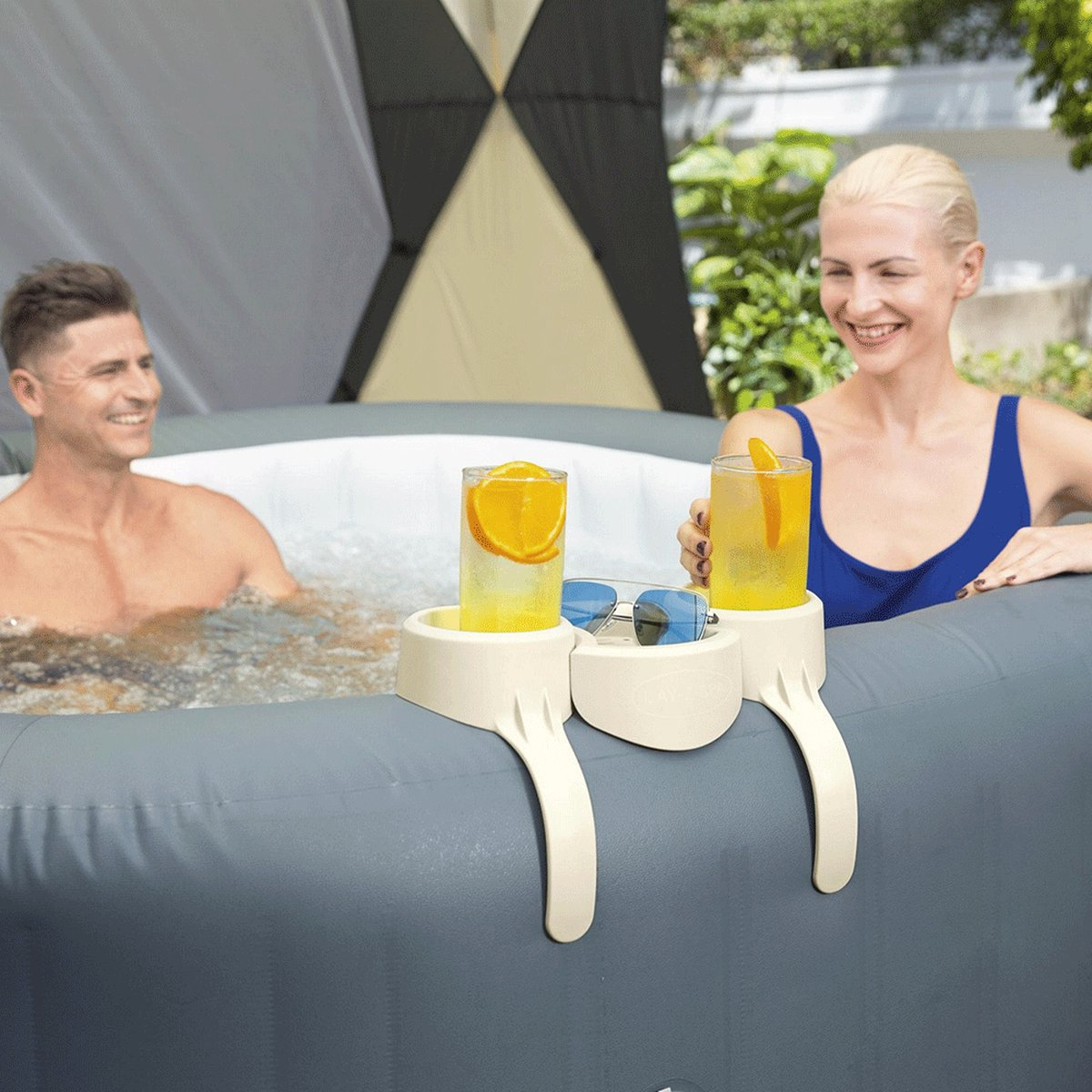 Een man en een vrouw zitten in een jacuzzi, elk met een drankje met sinaasappelschijfjes. Zonnebril op een dienblad ertussen.