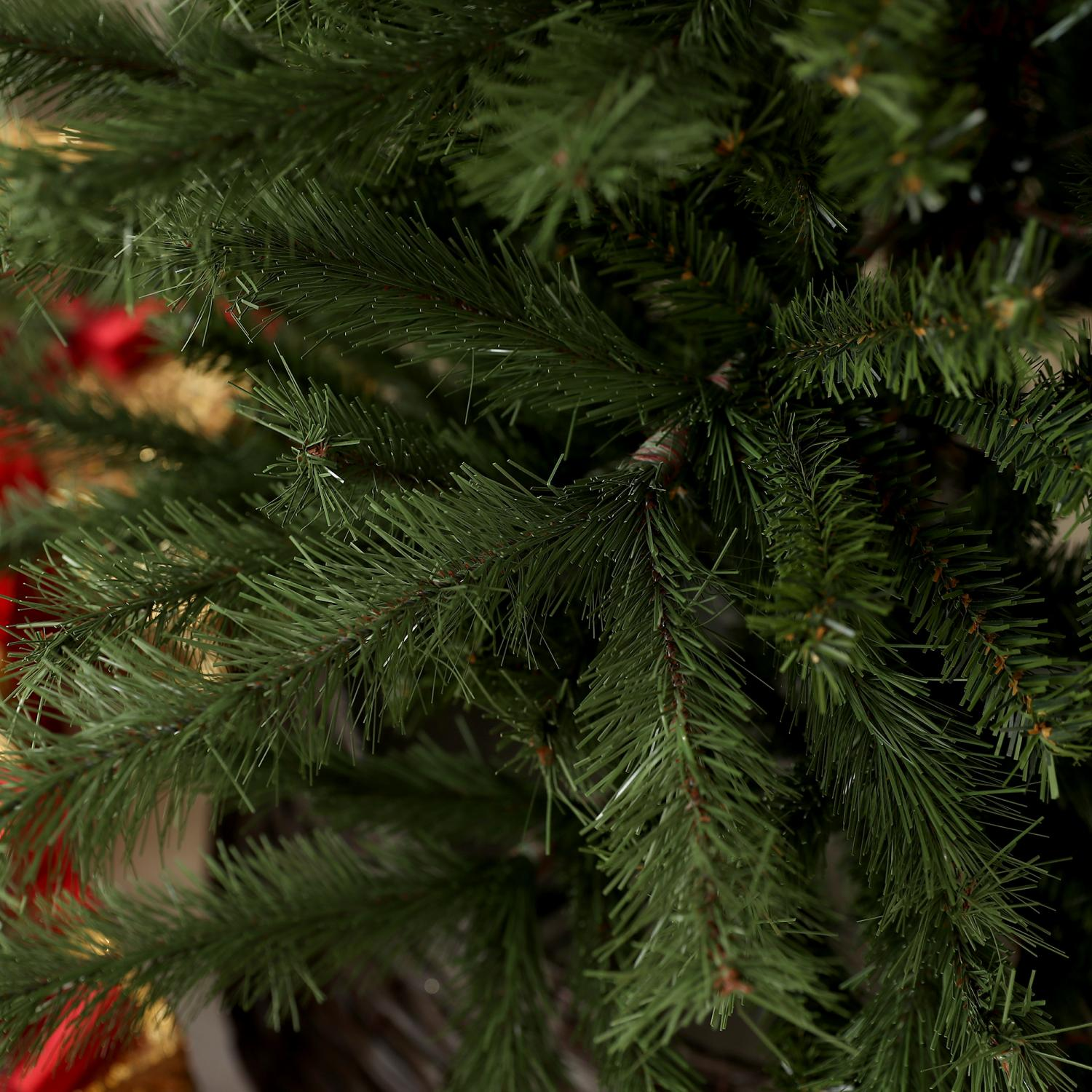 Nahaufnahme eines Weihnachtsbaums. Die Äste sind grün, mit vielen Nadeln. Rote und goldene Dekorationen sind im unscharfen Hintergrund sichtbar.