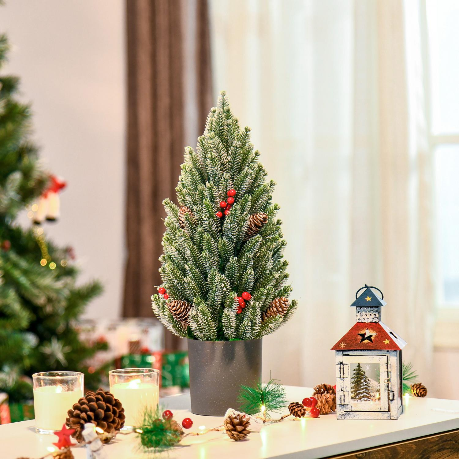 Ein kleiner Weihnachtsbaum mit Tannenzapfen und roten Beeren steht auf einem Tisch mit Kerzen und einer Laterne.