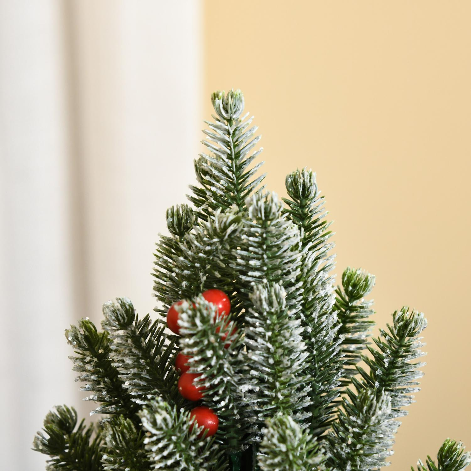 Nahaufnahme eines kleinen künstlichen Weihnachtsbaums mit roten Beeren. Der Baum ist grün mit weißen Spitzen, vor einem beigen Hintergrund.