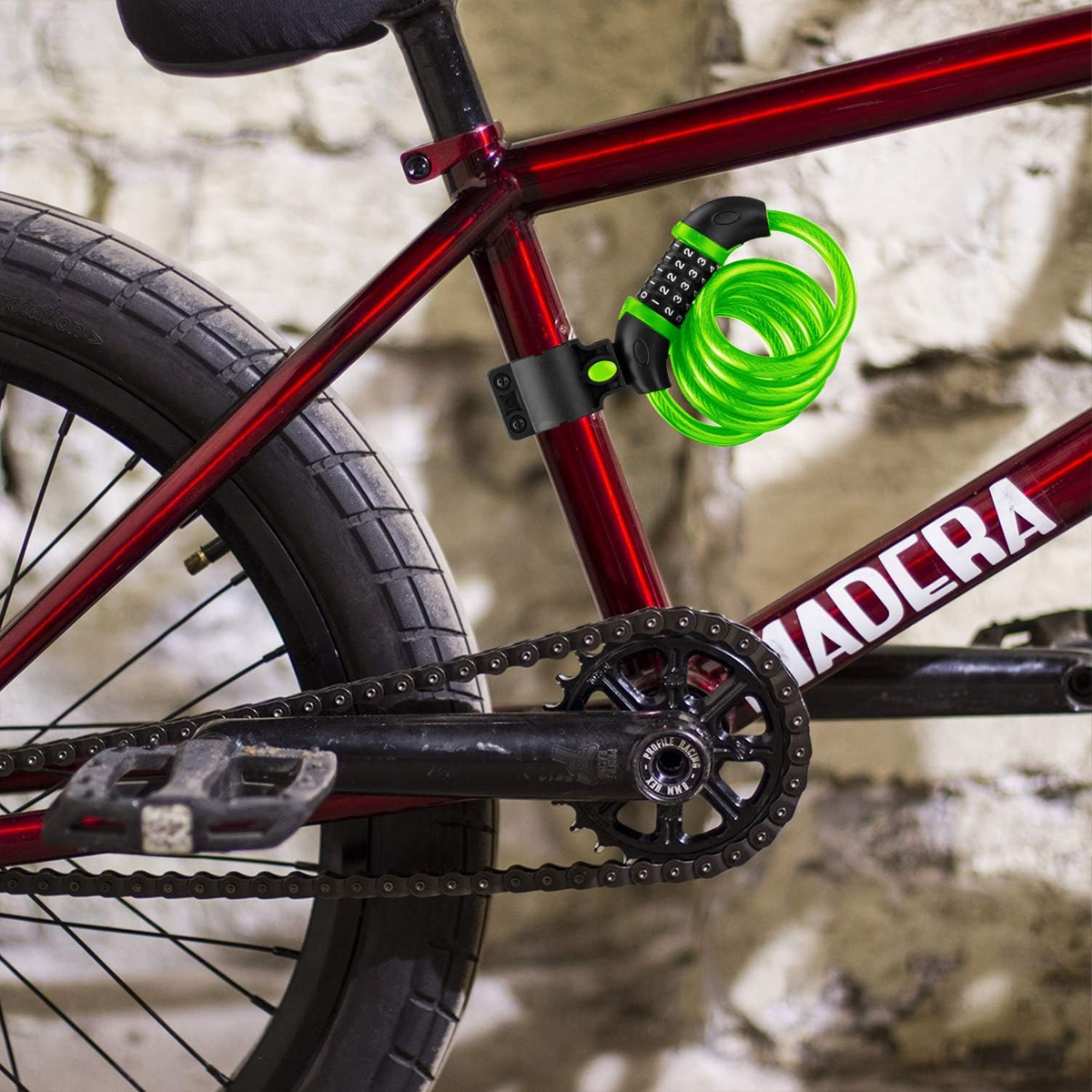 Ein rotes Fahrrad ist mit einem grünen Kabelschloss gesichert. Das Fahrrad hat eine schwarze Kette und Pedale. Der Hintergrund ist eine Steinmauer.