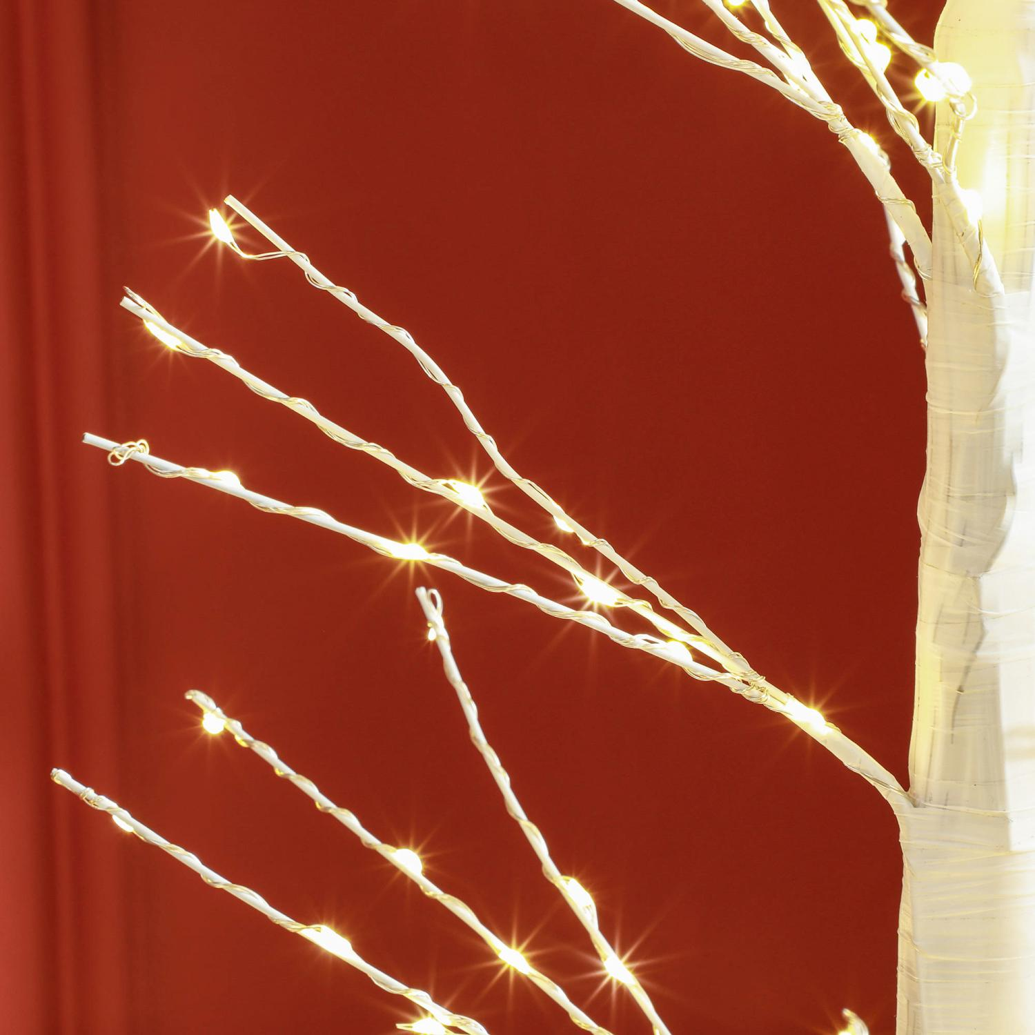 Ein weißer Zierbaum mit kleinen, leuchtenden Lichtern. Der Hintergrund ist ein sattes Rot, was eine festliche Atmosphäre schafft.