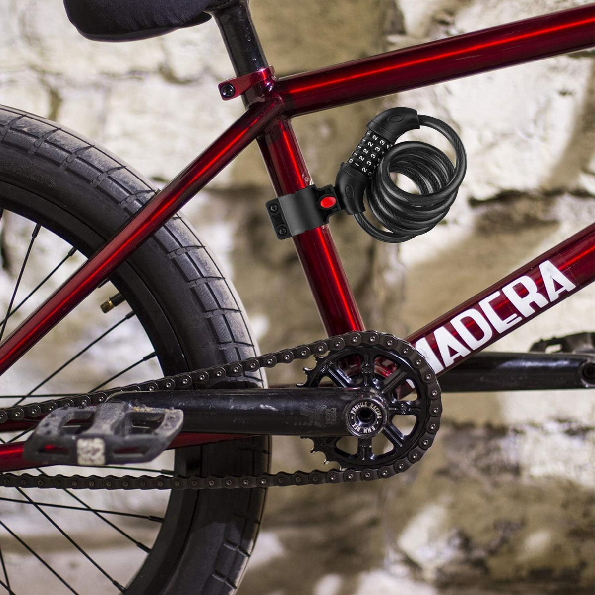 Rotes BMX-Fahrrad mit schwarzem Zahlenschloss. Das Fahrrad hat eine schwarze Kette und Reifen, vor einem Hintergrund aus Steinmauer.