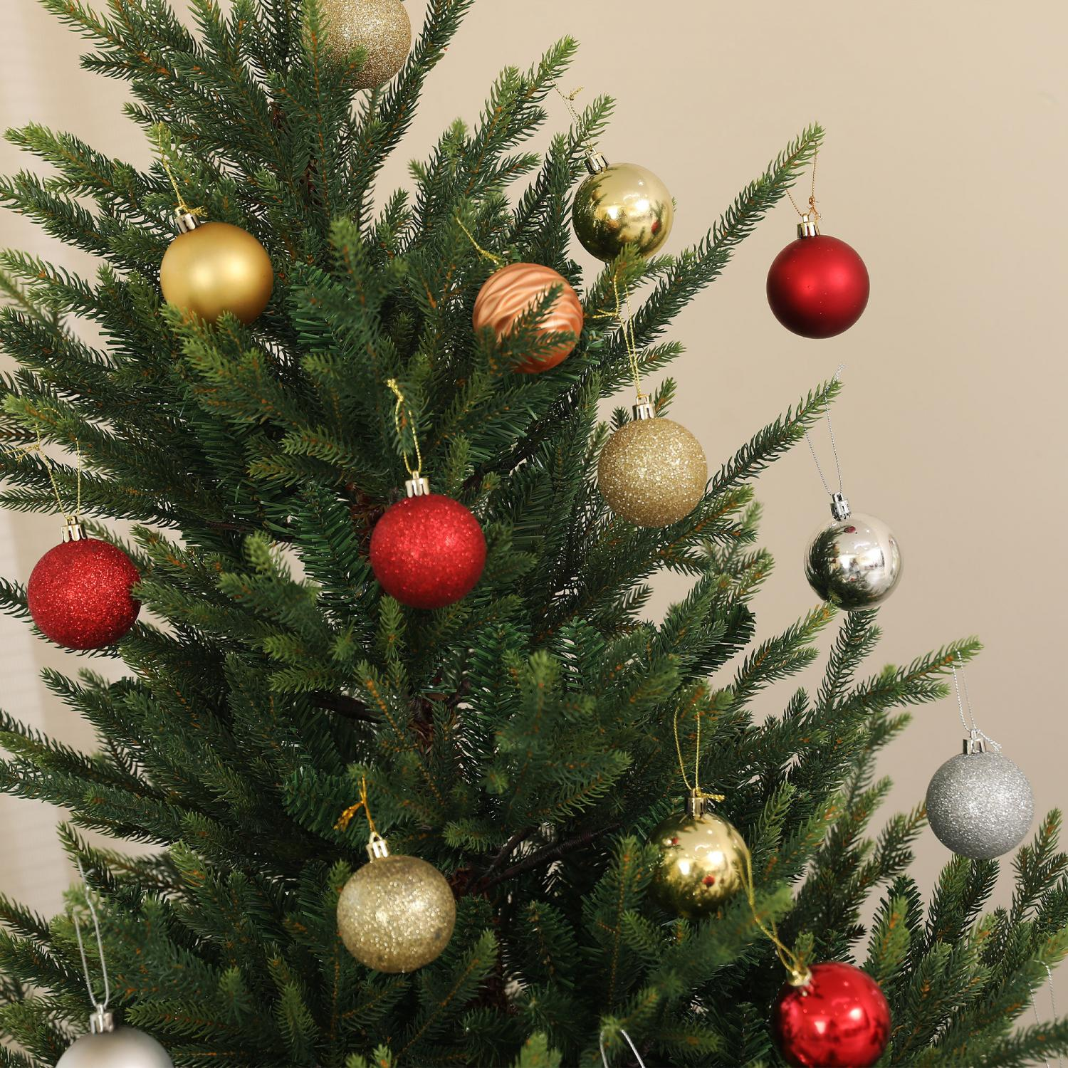 Ein Weihnachtsbaum ist mit mehreren Ornamenten in verschiedenen Farben geschmückt: Gold, Silber, Rot und Bronze. Der Hintergrund ist eine beige Wand.