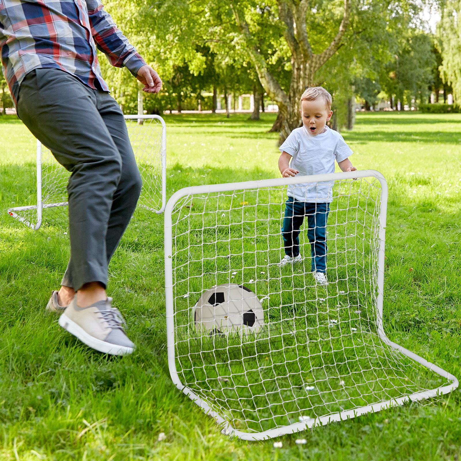 Un hombre patea una pelota de fútbol hacia una portería mientras un niño observa asombrado. La escena tiene lugar en un campo de hierba.