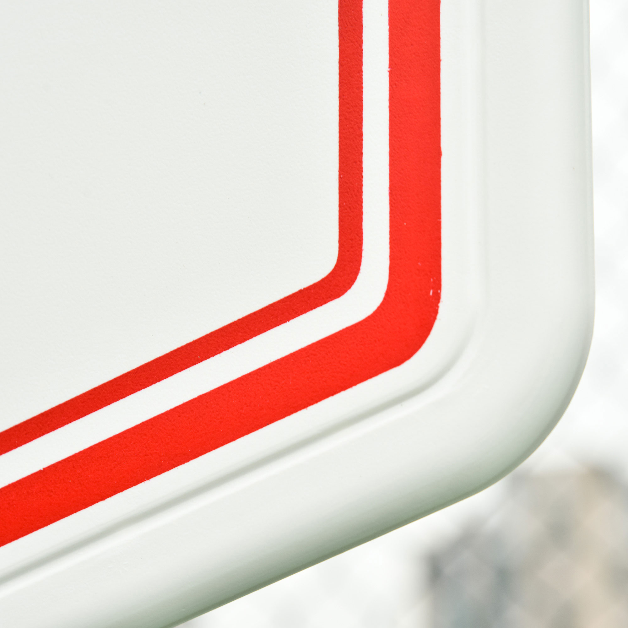 Primer plano muestra una superficie blanca con un borde rojo. La esquina es redondeada. Fondo desenfocado.